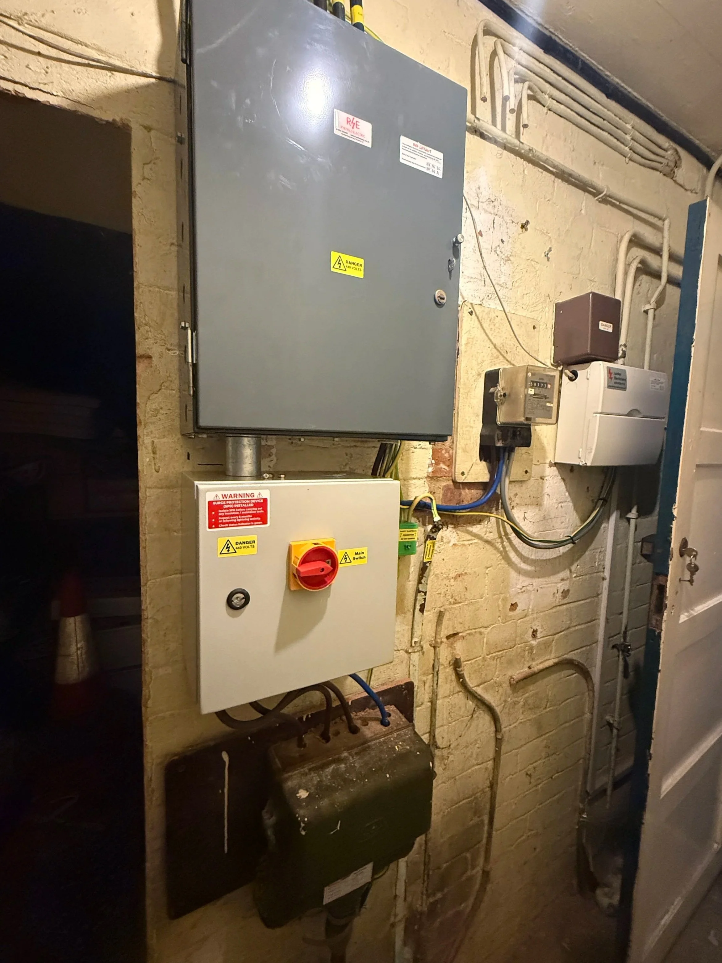 COMMERCIAL ELECTRICIAN Electrical control panels and wiring mounted on a brick wall in a utility room.