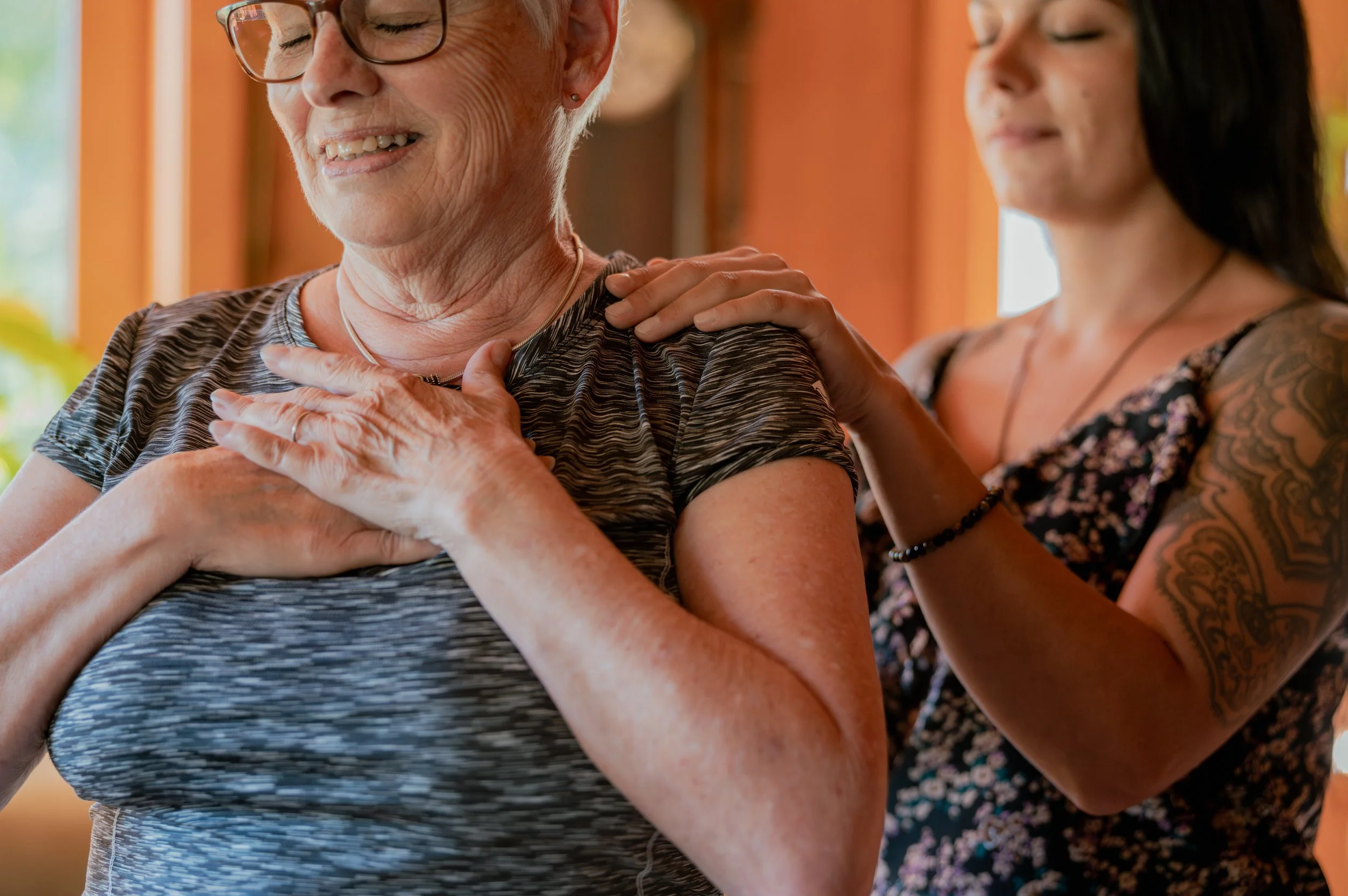 Zwei Frauen, eine ältere und eine jüngere, die zusammen eine Massage oder eine beruhigende Berührung im Innenraum eines Hauses genießen, mit warmem Licht im Hintergrund.