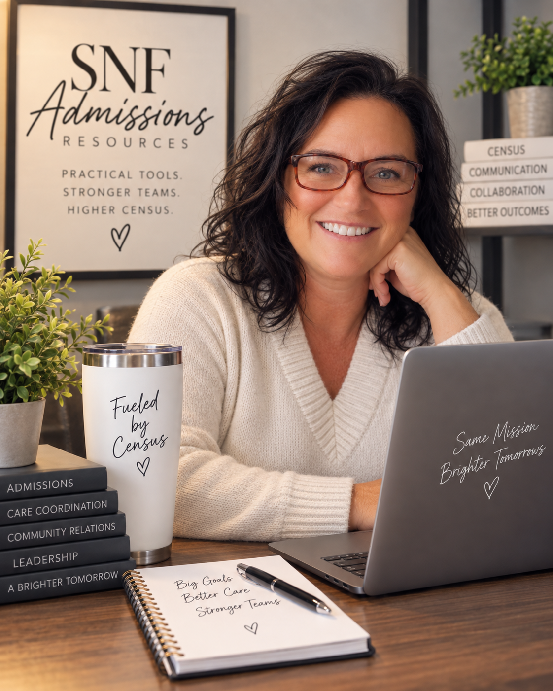Smiling woman with glasses sitting at a desk in an office, surrounded by books, a notebook, and a laptop, with posters and organization materials related to census and community relations in the background.
