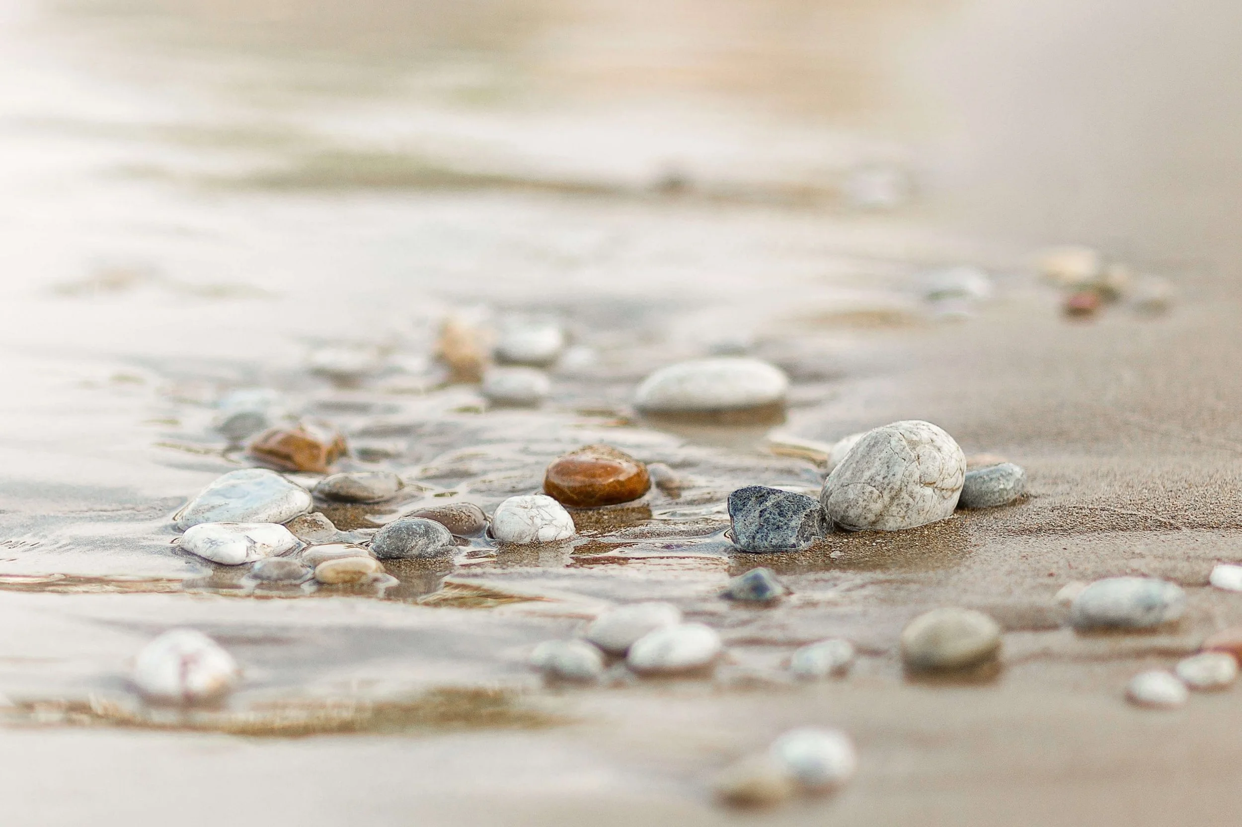 Close-up van kleurrijke kiezels op het strand bij de waterlijn, met lichte golven op de achtergrond.