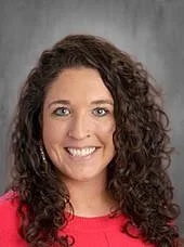 Portrait of a woman with curly brown hair, smiling, wearing a red top