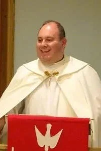 Man dressed in a white ceremonial robe standing behind a red podium.