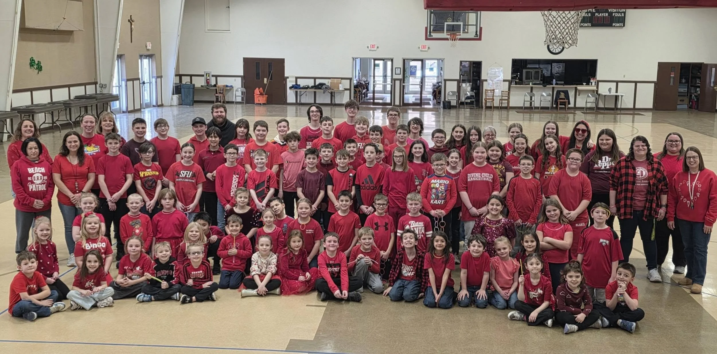 A large group of children and adults dressed in red, gathered in a gymnasium for a group photo.