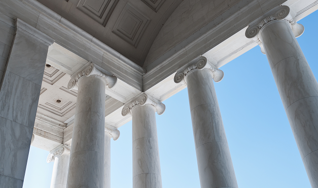 Close-up view of white marble columns supporting a classical building's portico against a blue sky.