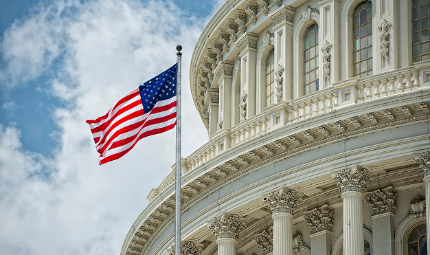The United States Capitol building with an American flag flying in front of it under a cloudy sky.