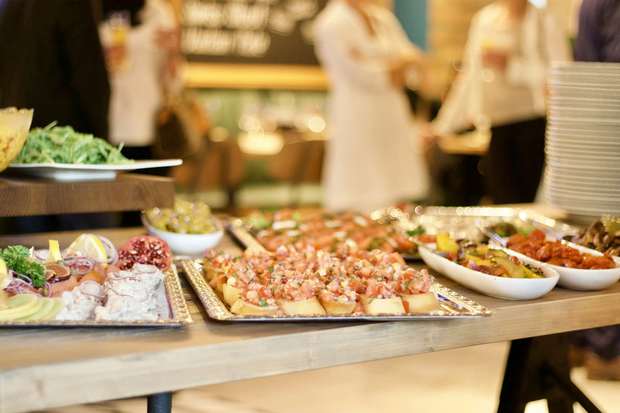 Assorted appetizers and salads on a table at a buffet with people in the background.