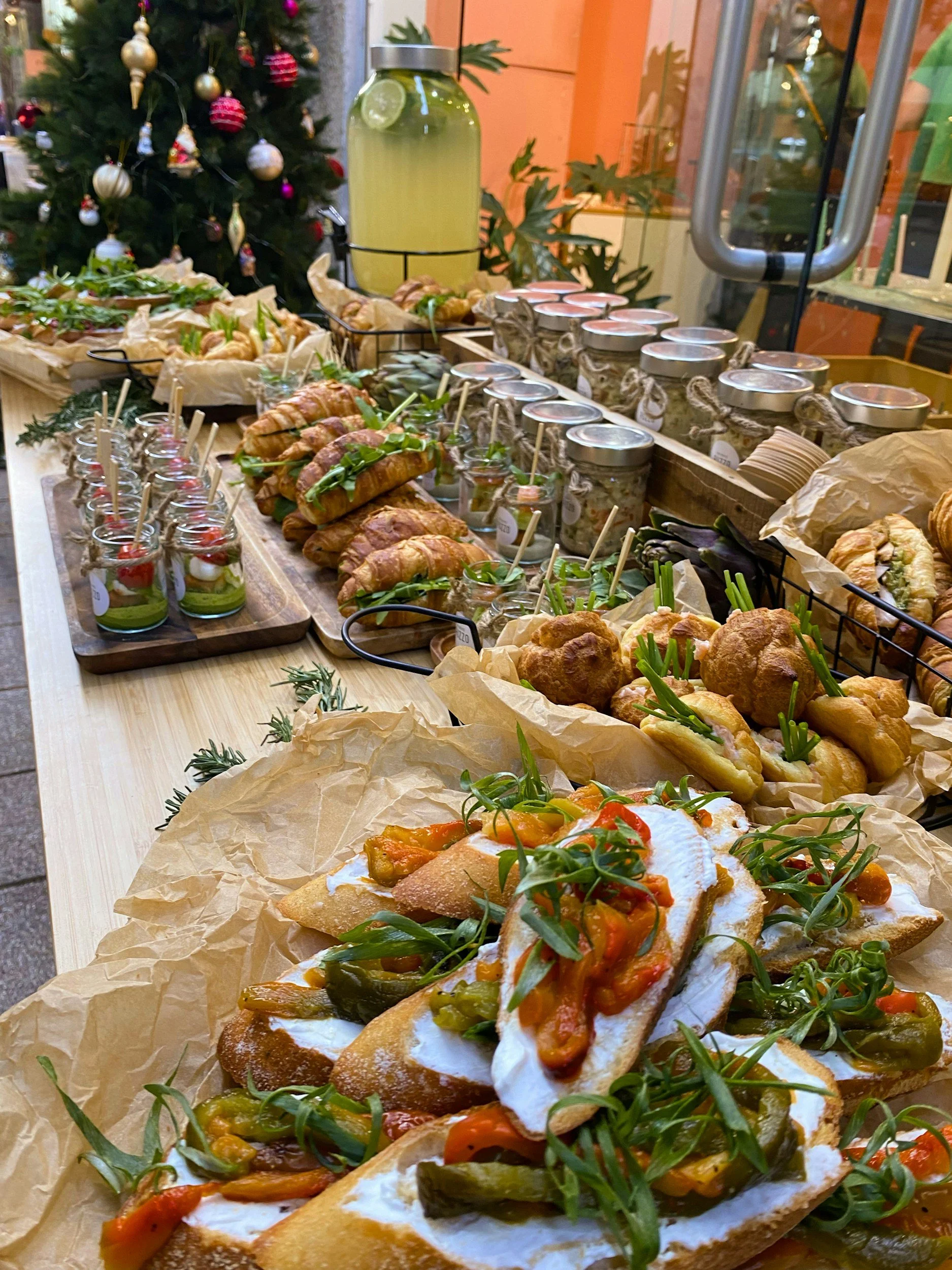 Italian food spread with open-faced sandwiches topped with vegetables, cheese, and herbs on parchment paper, with a Christmas tree in the background.