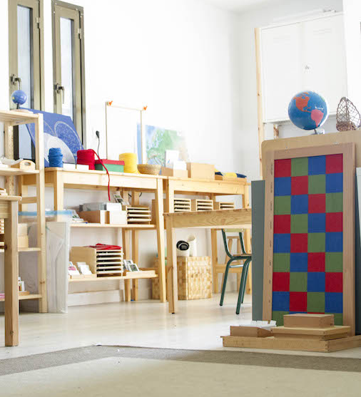 A classroom with wooden furniture, educational materials, a globe, and colorful decor.