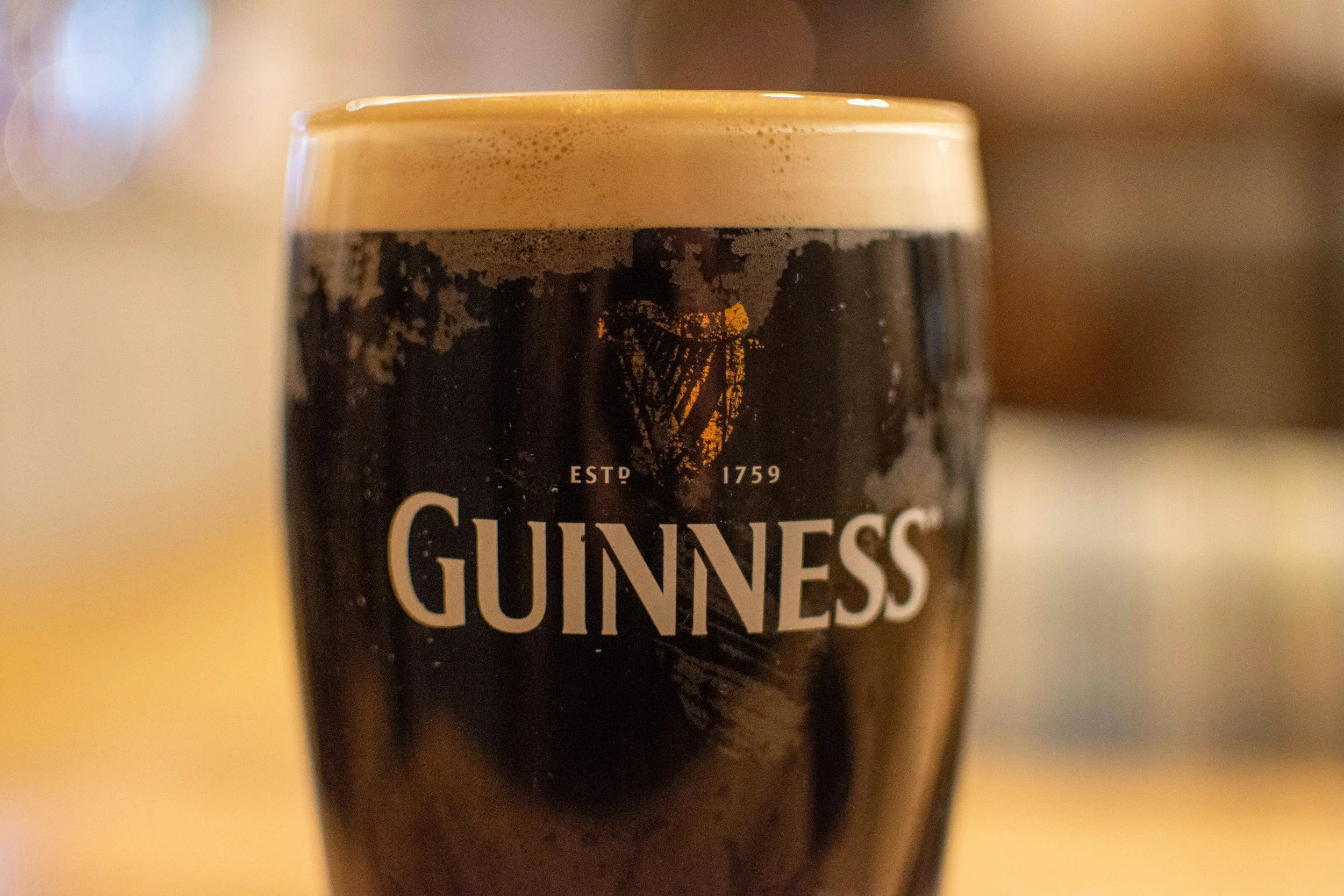 Close-up of a glass of Guinness stout beer with a creamy foam head, featuring a dark body and the Guinness logo.