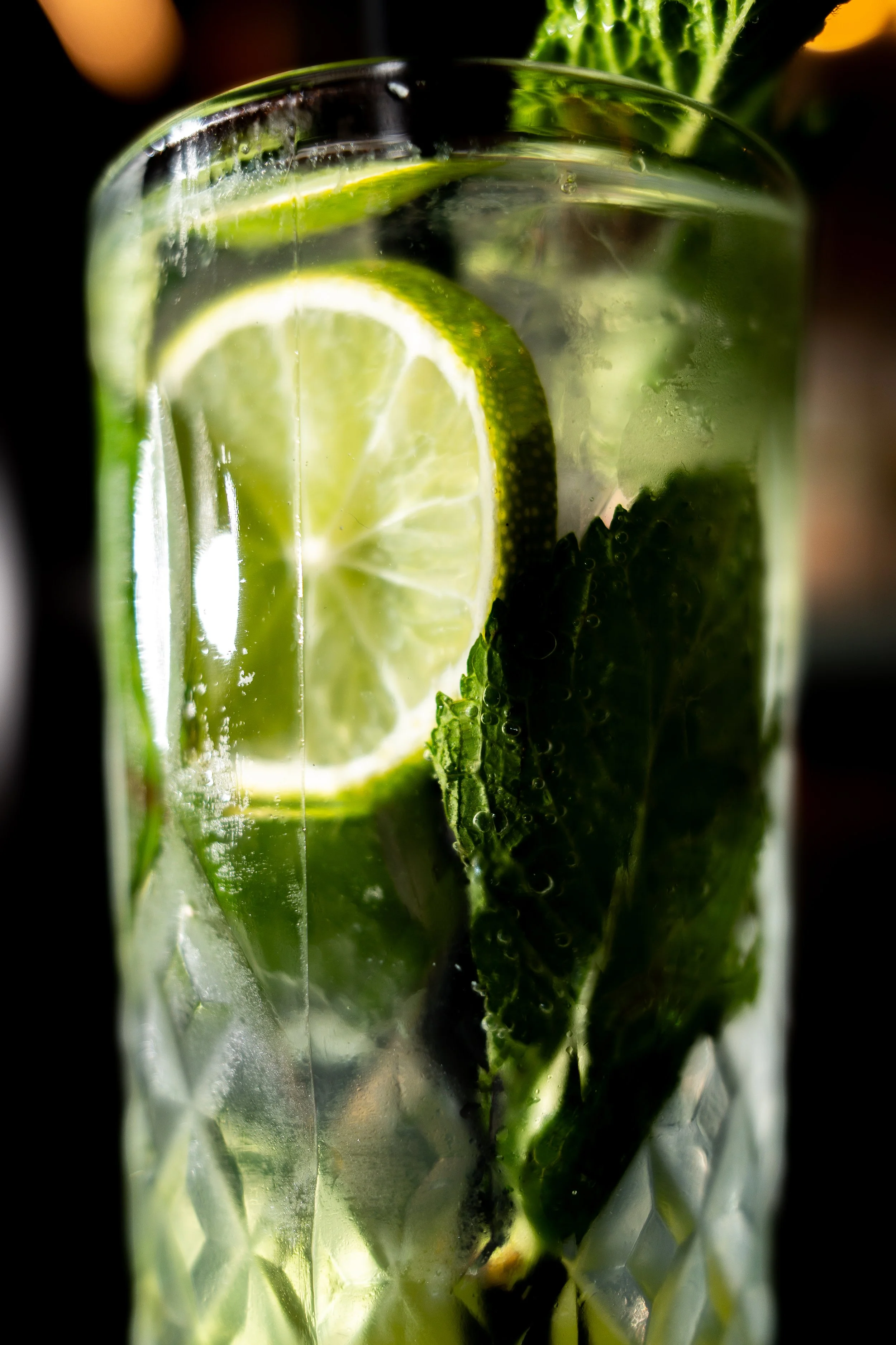 Close-up of lime slices and mint leaves in a glass of sparkling water.