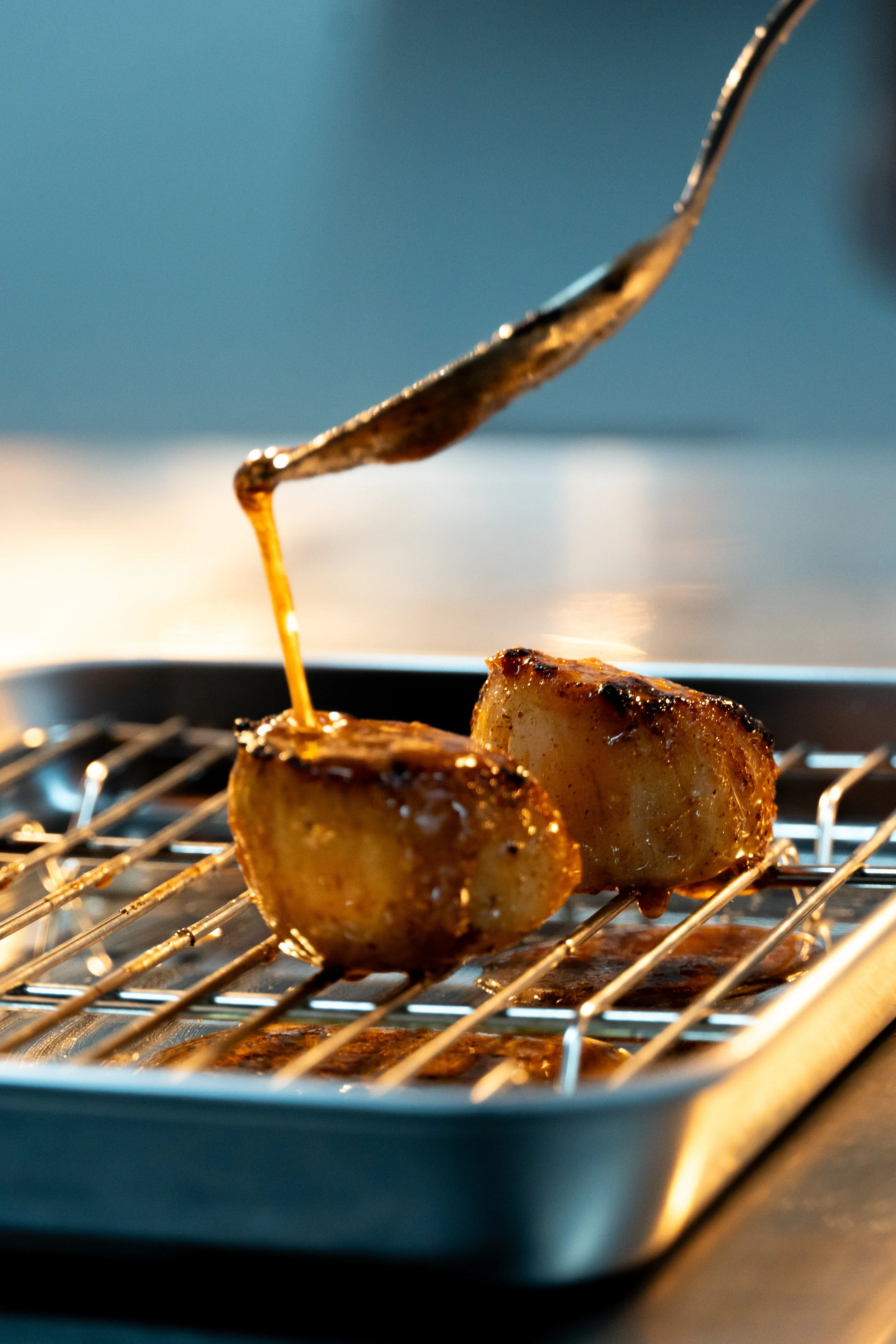 Close-up of chicken pieces on a barbecue grill with barbecue sauce dripping from a fork.