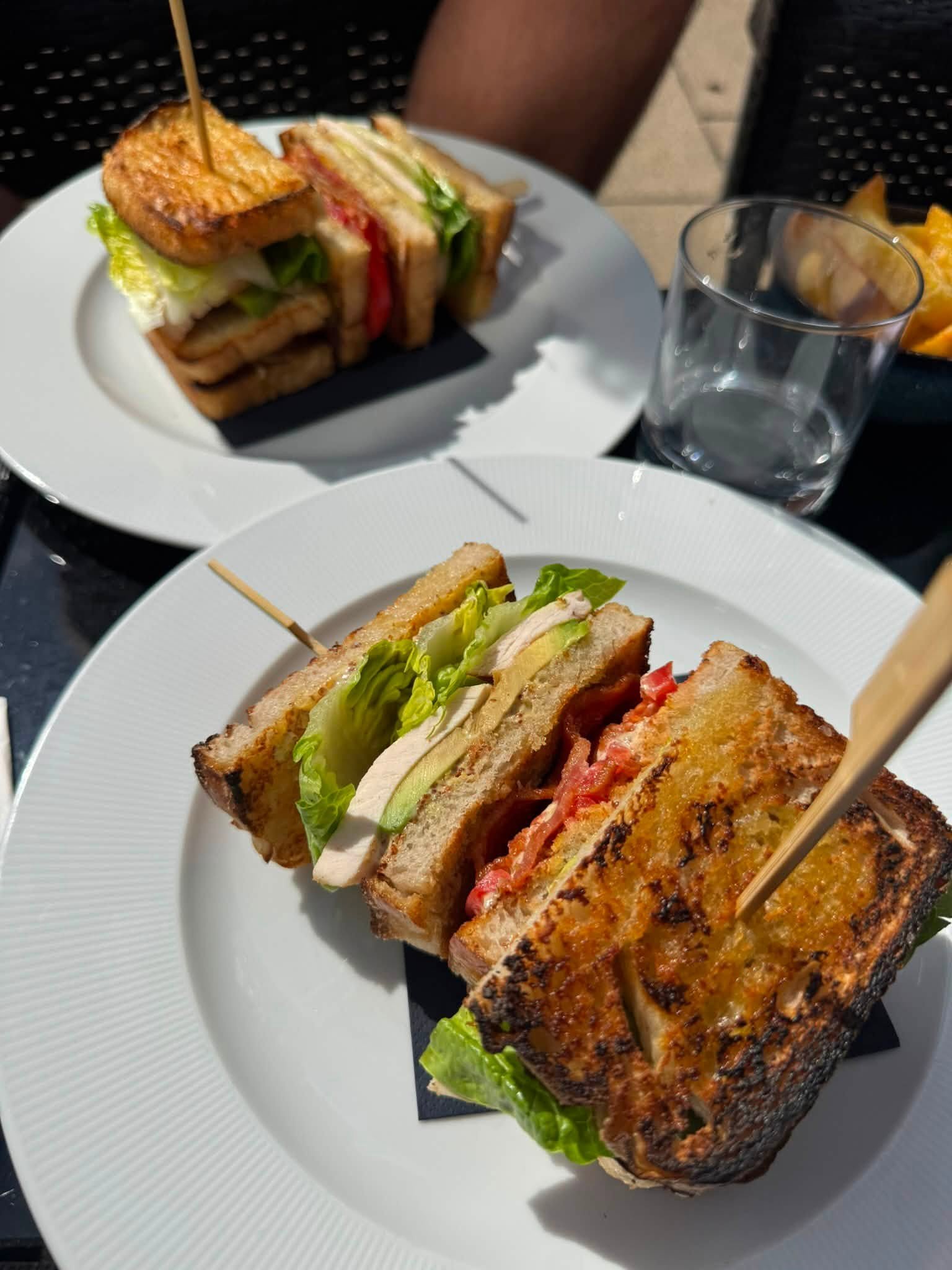 Close-up of a grilled sandwich with lettuce, tomato, and cheese on toasted bread, served on a white plate.
