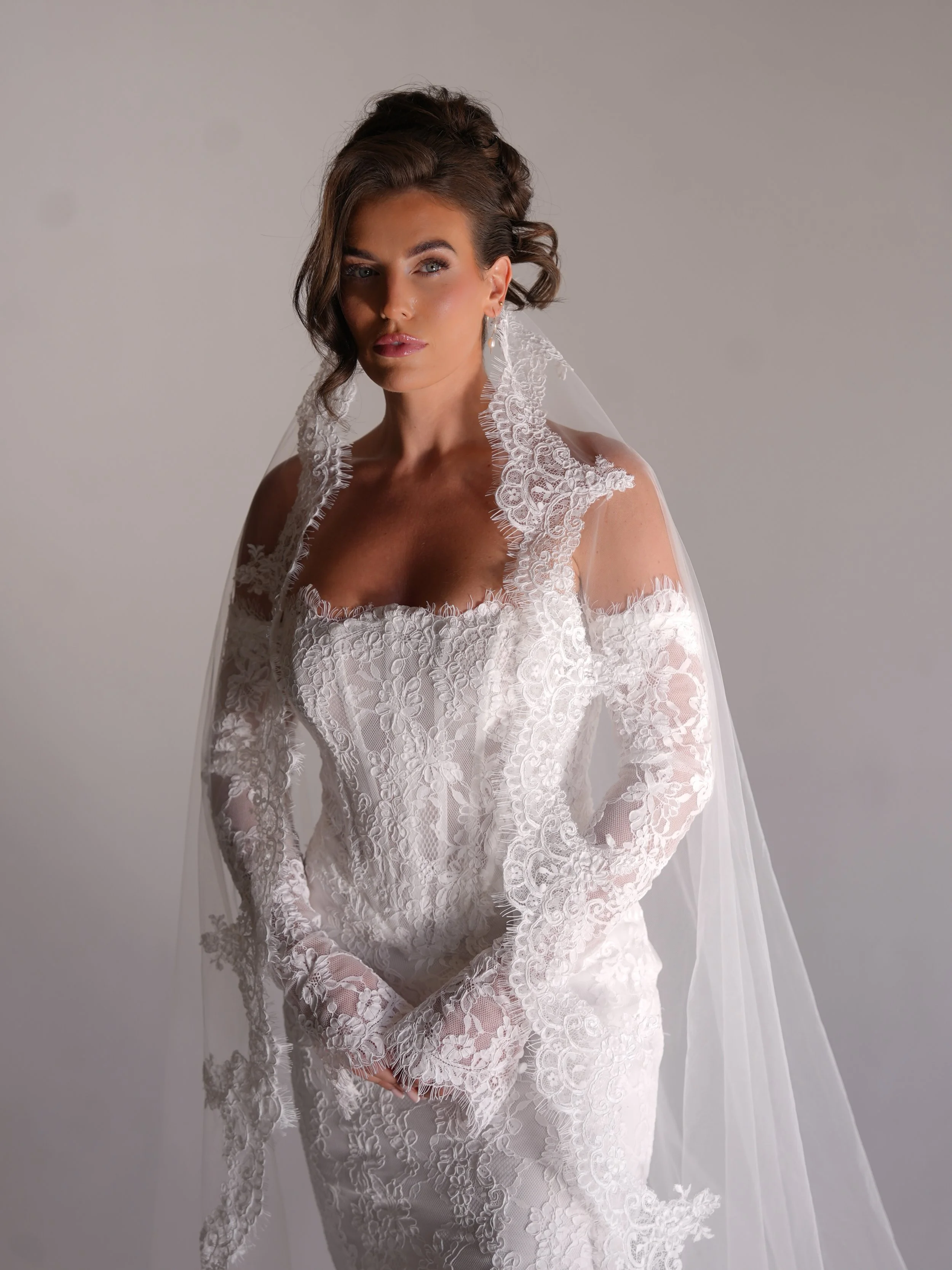 Bride in a lace long sleeve wedding dress and matching veil posing for a luxury wedding photographer