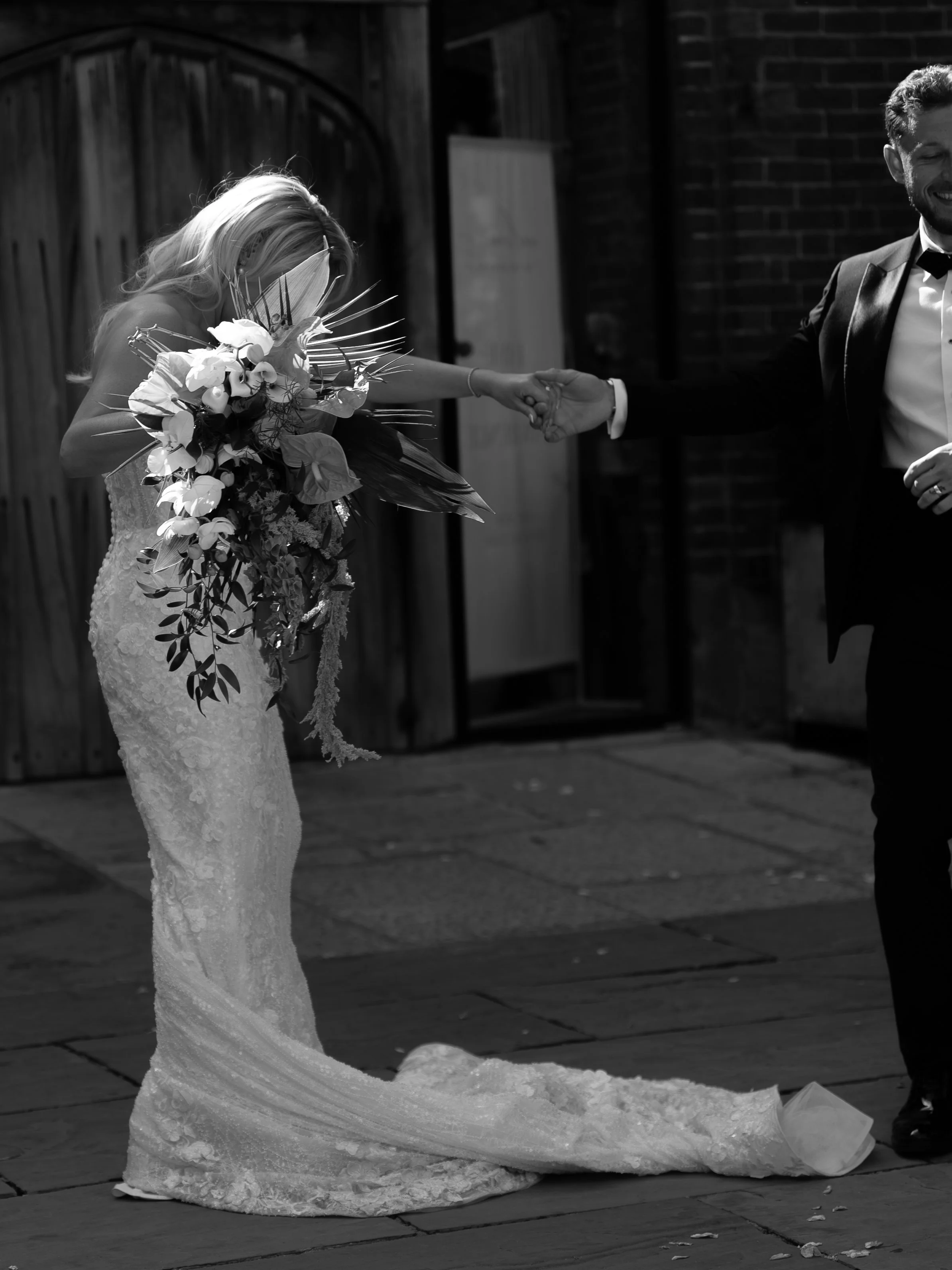 A bride in a wedding dress holding a bouquet, with a long train, dancing with a groom dressed in a tuxedo.