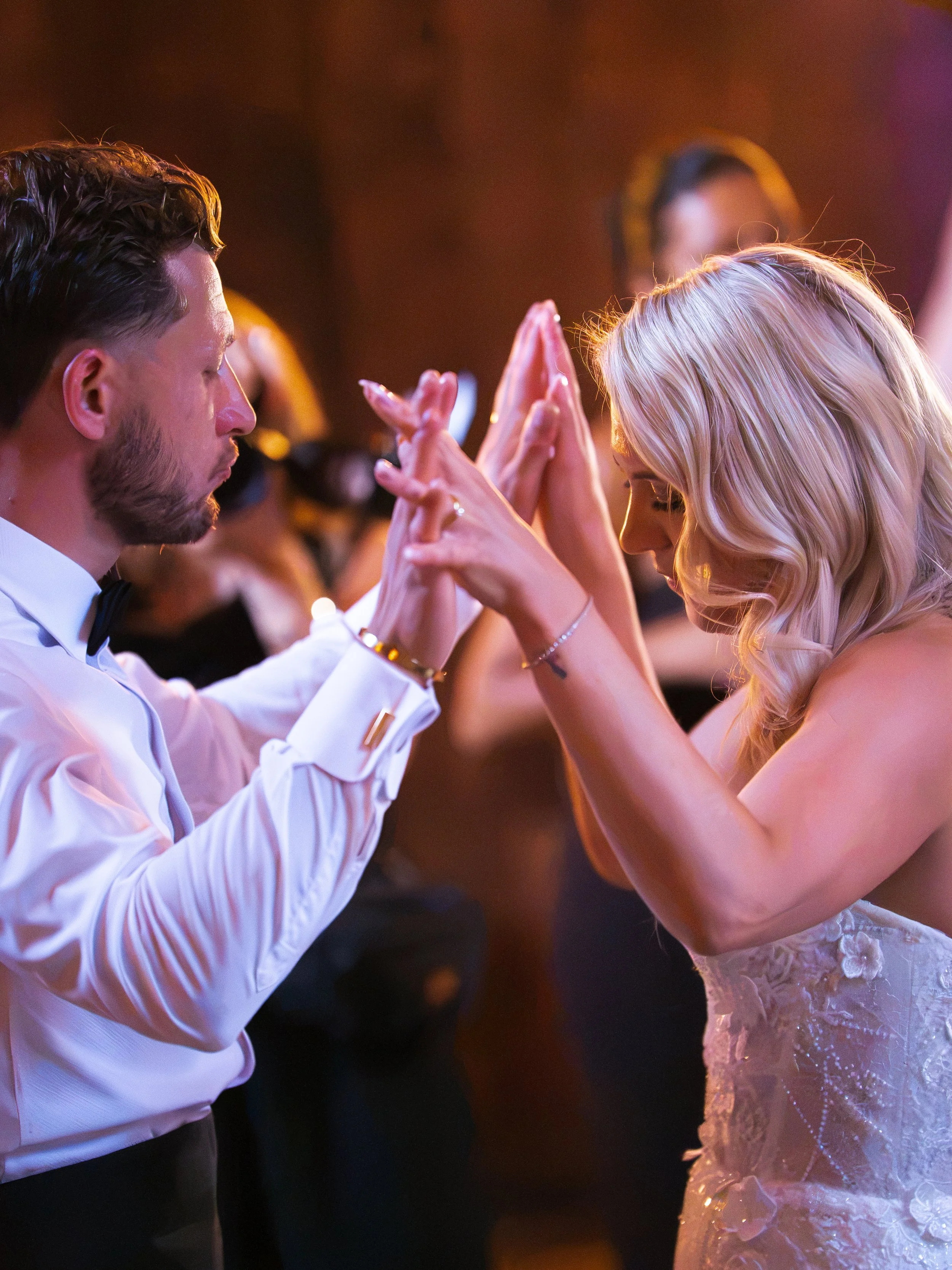 A bride and groom dancing closely together at their wedding reception, with both holding hands together and leaning their foreheads against each other in a romantic moment.