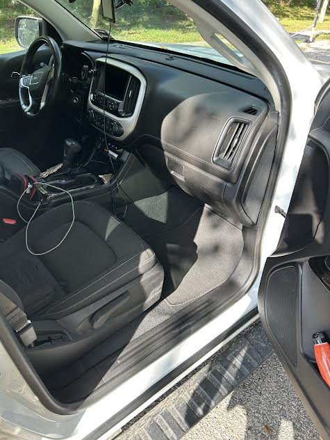 Inside view of a vehicle's front passenger seat and dashboard, with the door open, showing the steering wheel, dashboard controls, and a charging cable.