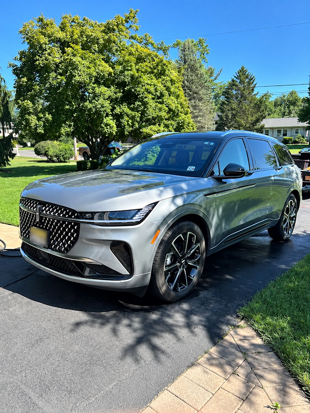 Gray SUV parked on driveway in front of a green lawn with trees under a sunny blue sky.