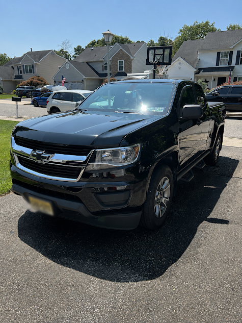 Black Chevrolet pickup truck parked on a driveway in a suburban neighborhood with houses and other vehicles in the background.