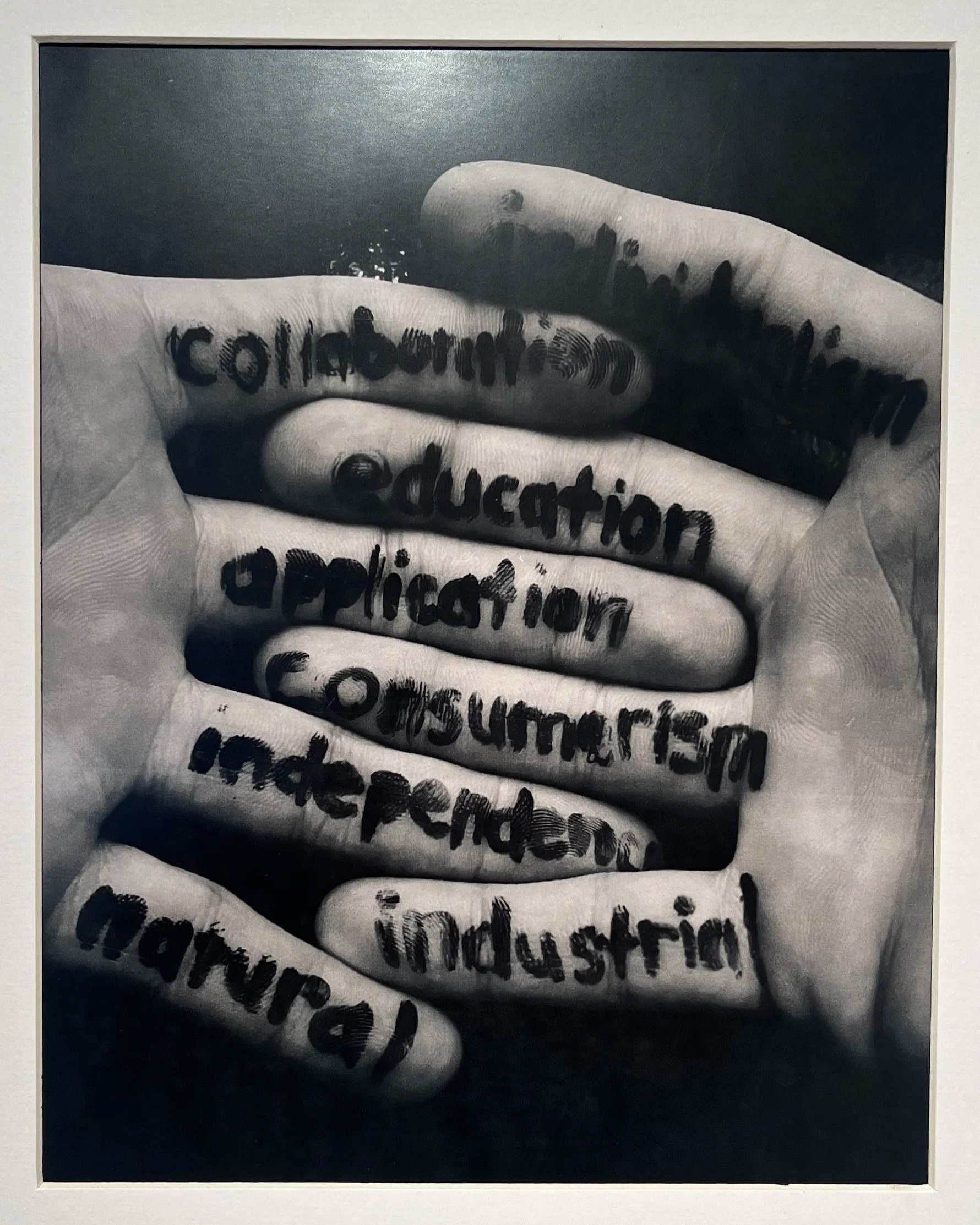 Black and white photo of four fingers with words written on them, including 'colonization' and 'education', with some of the fingers darkened or stained.