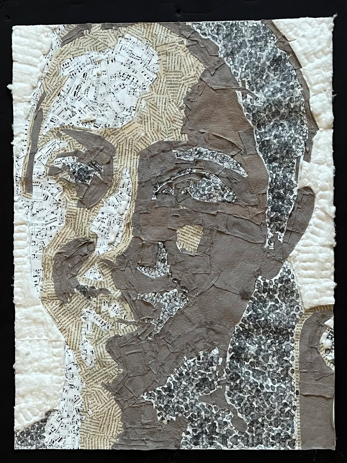 A collage of various textured and colored torn paper pieces arranged to form an abstract design on a dark background. The paper includes pages with printed musical notes, text, and patterned designs in shades of white, beige, brown, and black.