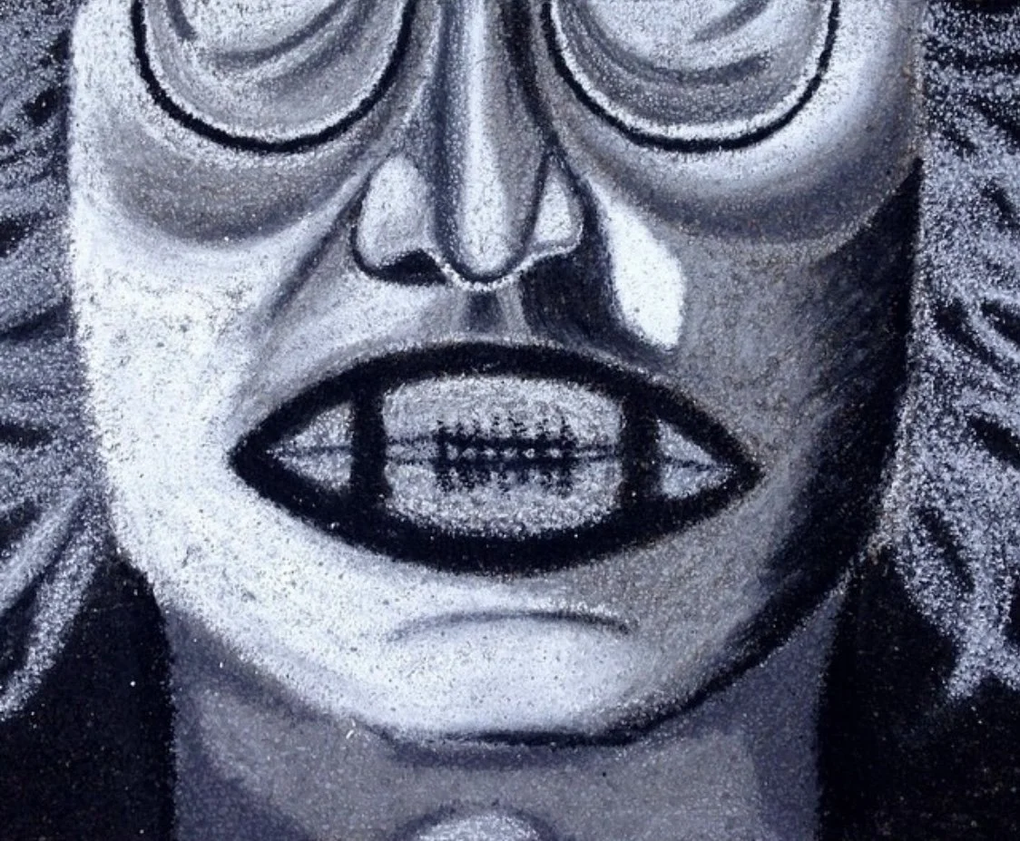 Close-up of a monochrome spray-painted portrait of a person's face with a wide-open mouth, exaggerated lips, and detailed features.
