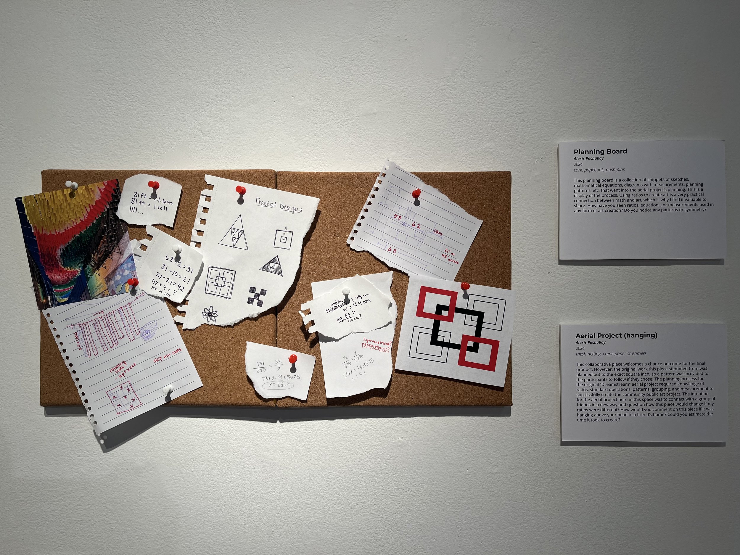 A cork bulletin board with various torn paper notes, sketches, and diagrams pinned to it, alongside informational plaques on the right side of the display.