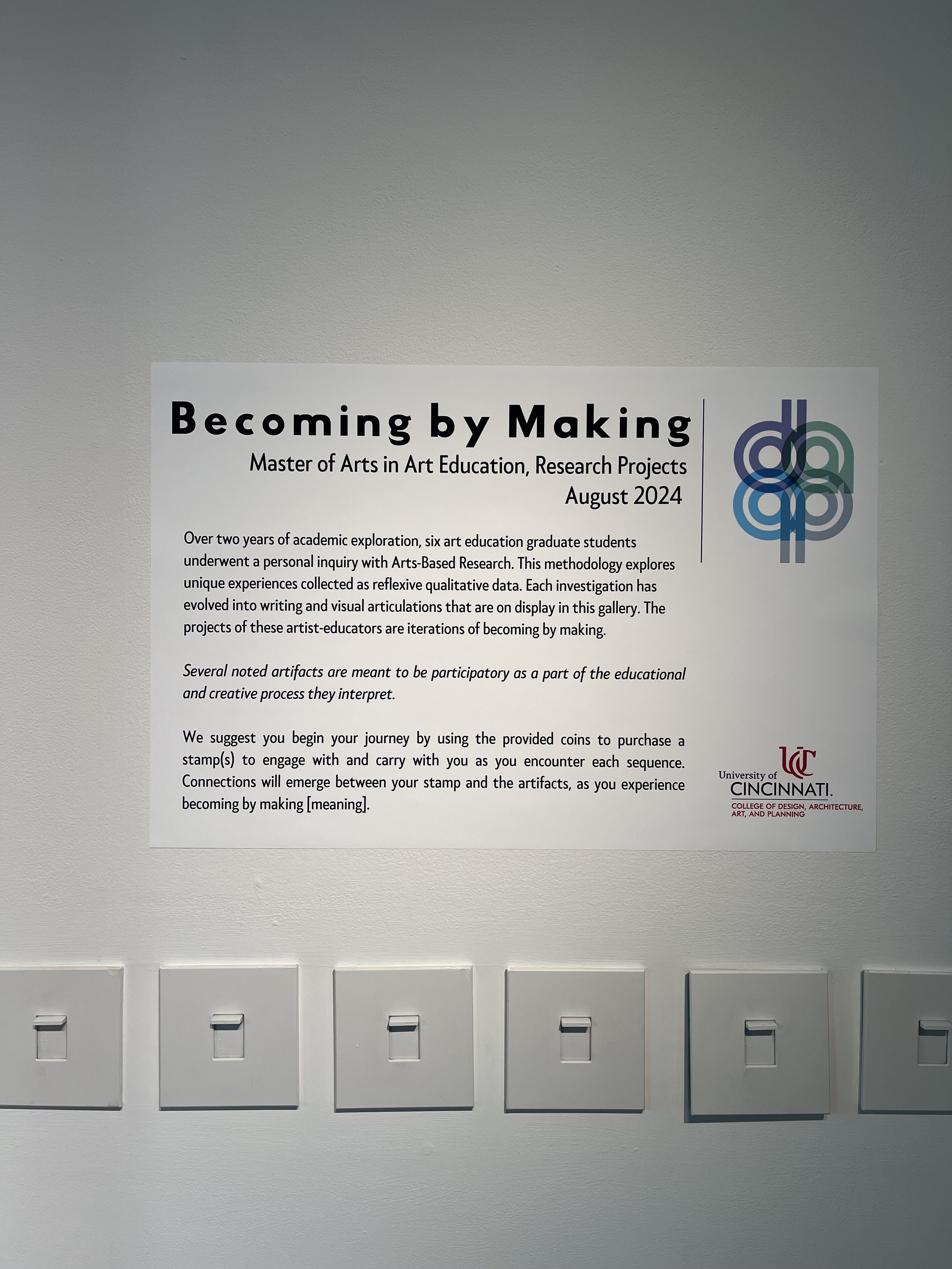 A poster on a wall titled "Becoming by Making," promoting a Master of Arts in Art Education, Research Projects, August 2024. The poster discusses a two-year academic exploration involving six graduate students using Arts-Based Research, with artifact