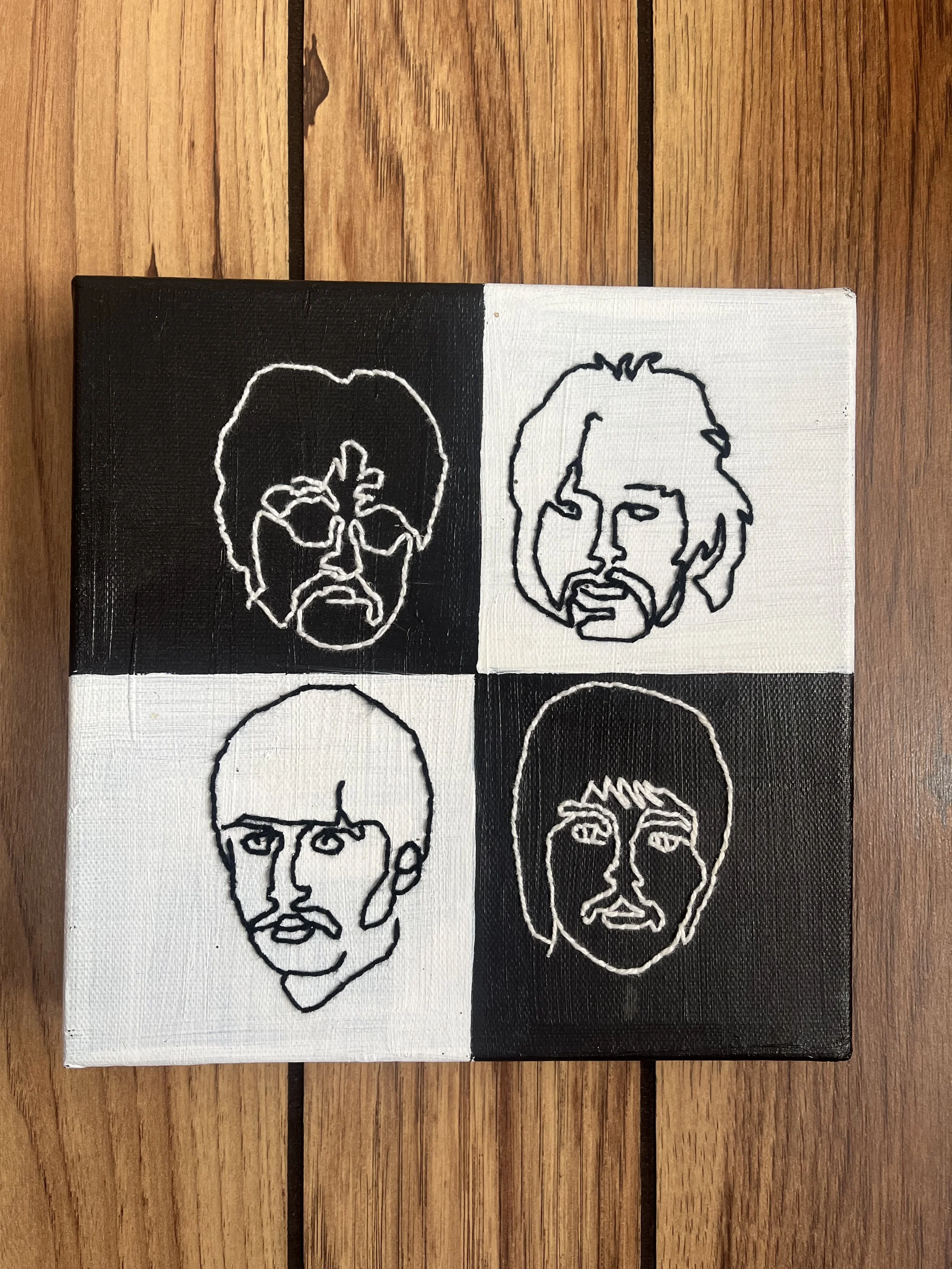Four small square canvas artworks with minimalist black and white line portraits of different people's faces, arranged in a 2x2 grid on a wooden surface.