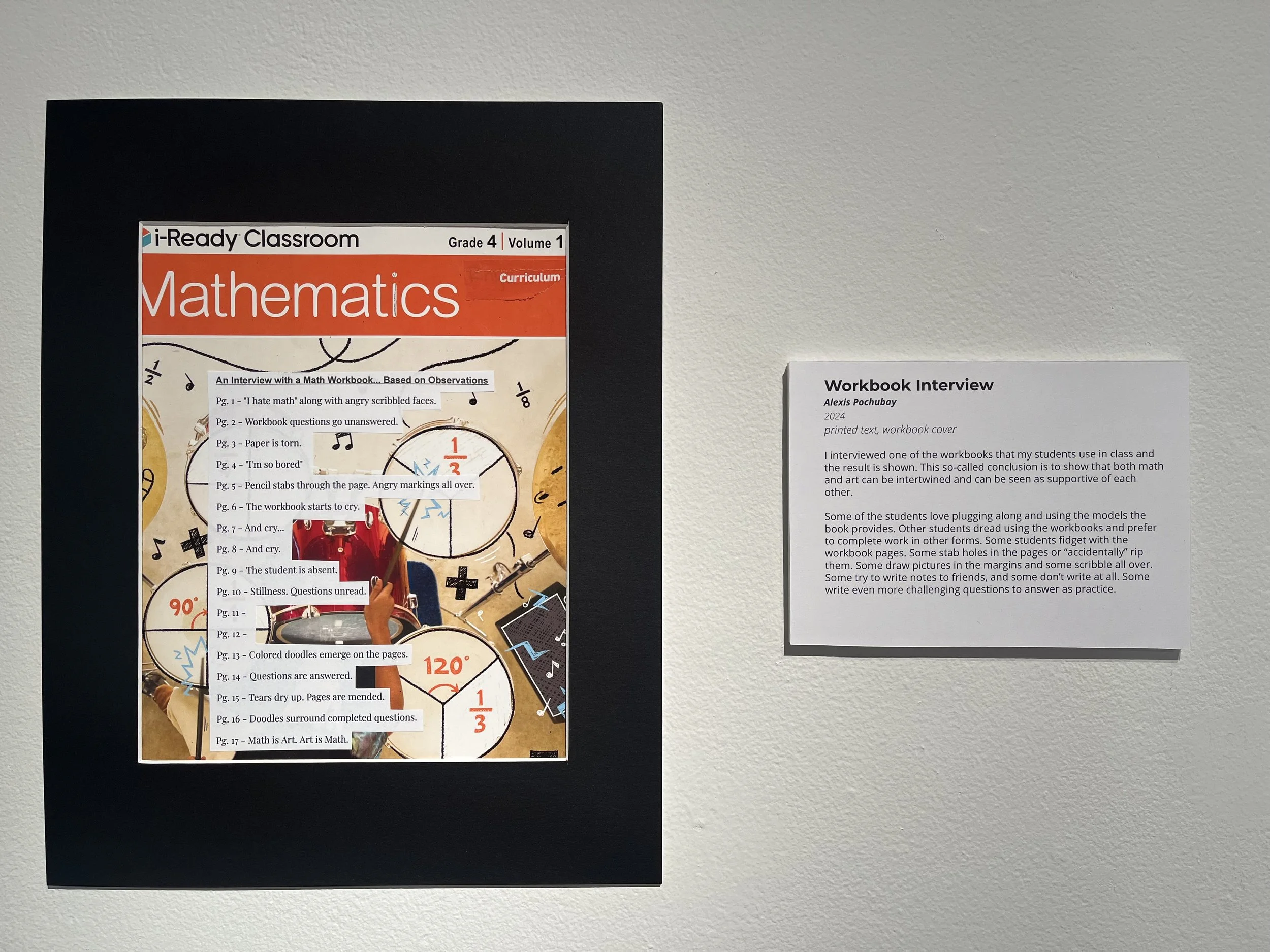 A classroom display featuring a mathematics workbook cover titled "i-Ready Classroom Grade 4 Volume 1 Curriculum" with handwritten annotations pointing to various pages and questions. Next to it, a separate printed sheet titled "Workbook Interview" p