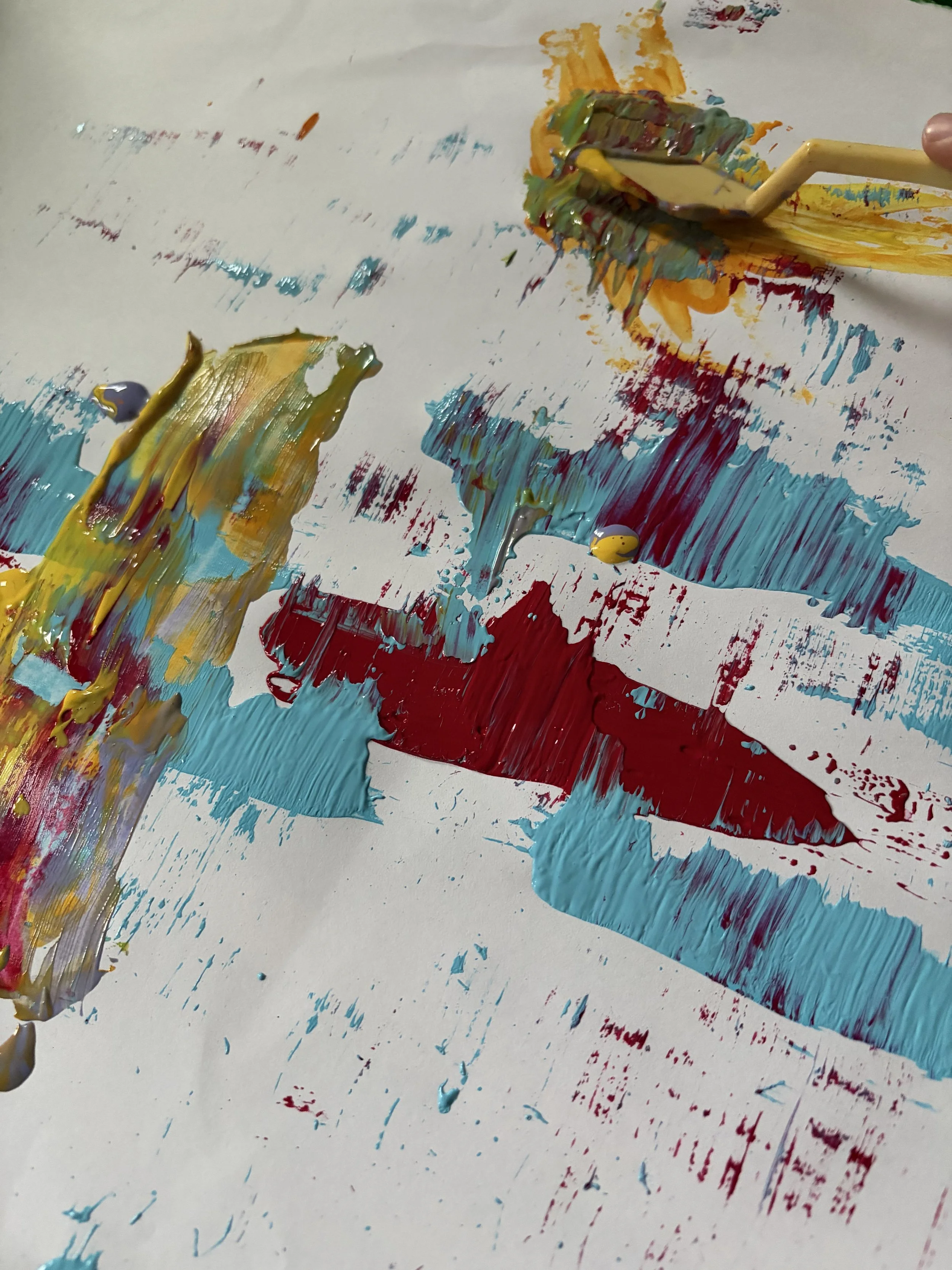 A sheet of paper with colorful thick paint strokes in yellow, blue, red, green, and orange, created using a wooden stick and a palette knife.