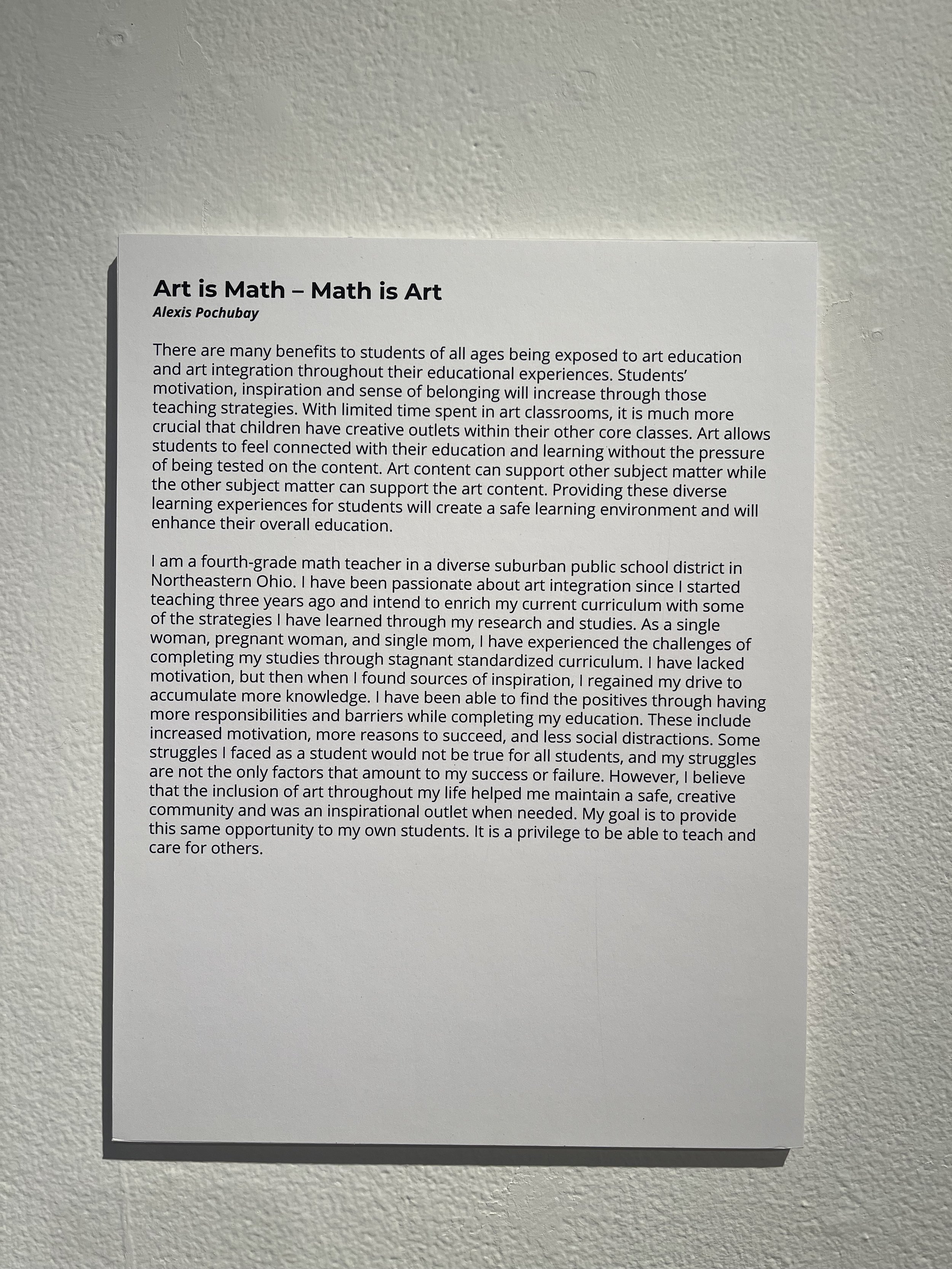 A printed paper on a white wall titled 'Art is Math — Math is Art' by Alexis Pochubay, discussing the connection between art and mathematics, benefits of art education, and the author's background as a math teacher in Ohio.