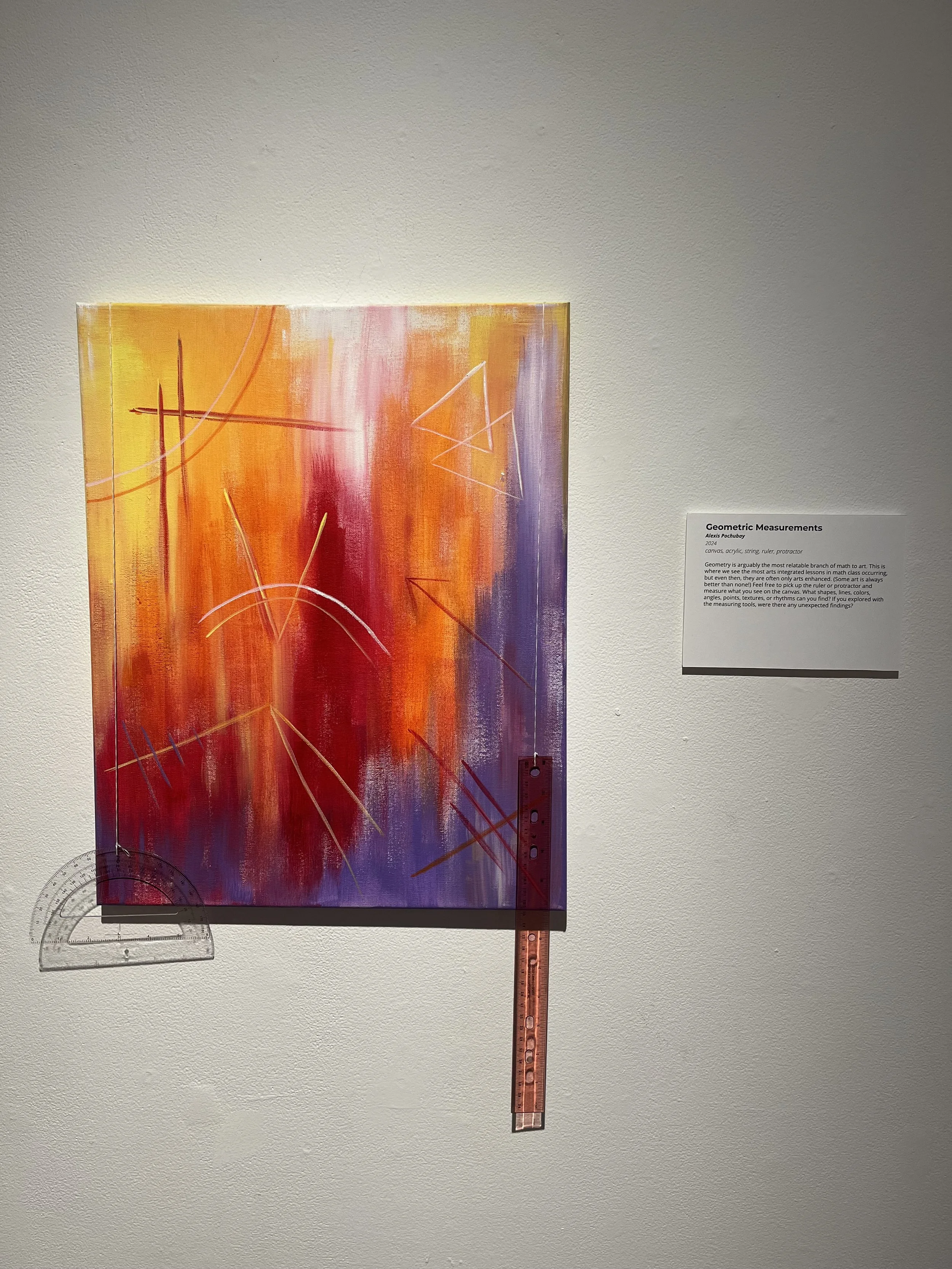 Abstract painting with vertical red, orange, yellow, and purple brushstrokes, overlaid with geometric white lines and shapes. A clear ruler and protractor are placed on the artwork in an exhibition setting.