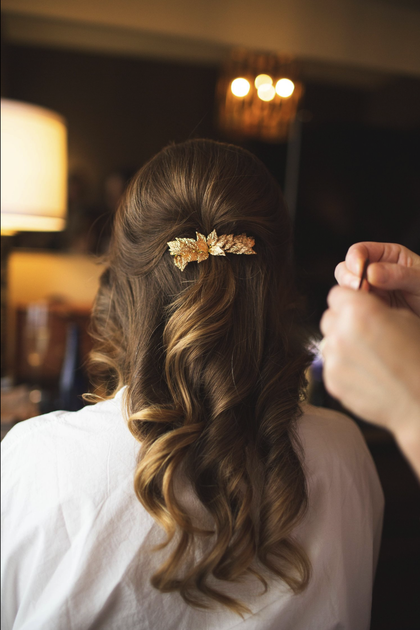 A woman with newly styled hair decorated with a gold leaf hair clip, in the process of getting her hair done.