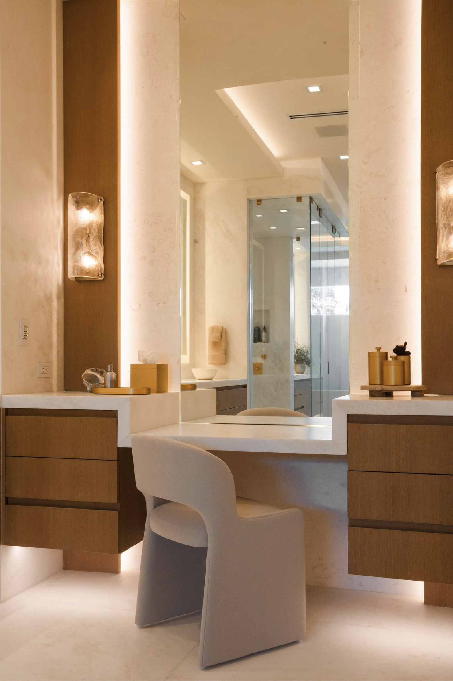 Modern interior space with a large mirror, a white chair, wooden cabinetry, and decorative objects such as vases and small sculptures. Soft lighting and neutral tones create an elegant atmosphere.
