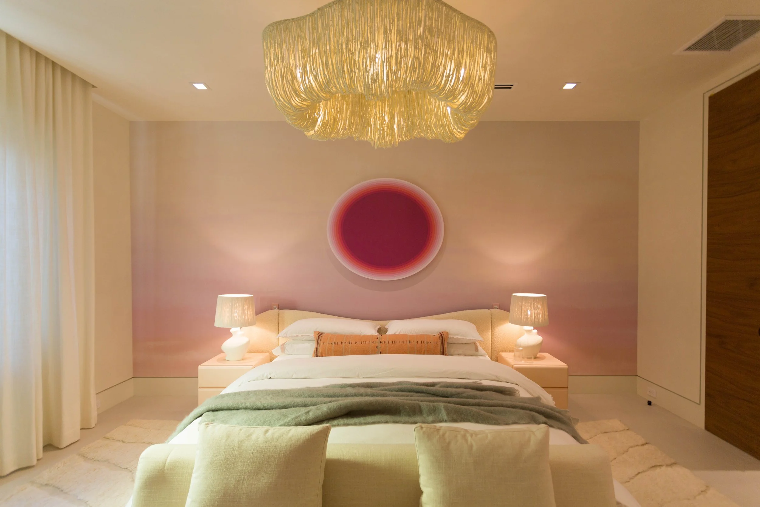A modern bedroom with a bed, two nightstands with lamps, and a decorative wall hanging above the bed, illuminated by warm lighting.