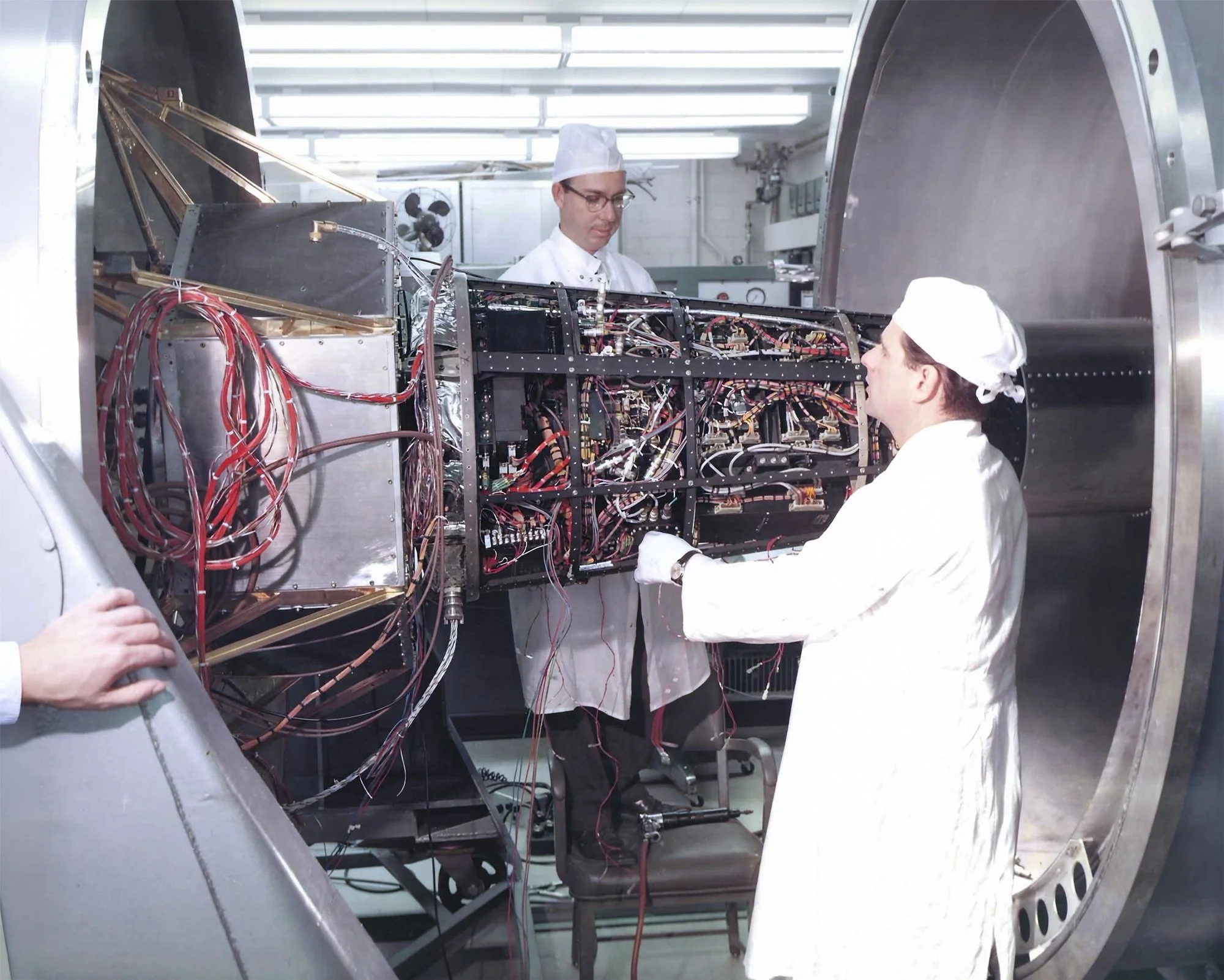 Scientists working on the wiring and electronics inside the spherical structure of a space telescope or satellite, with metal and copper components.