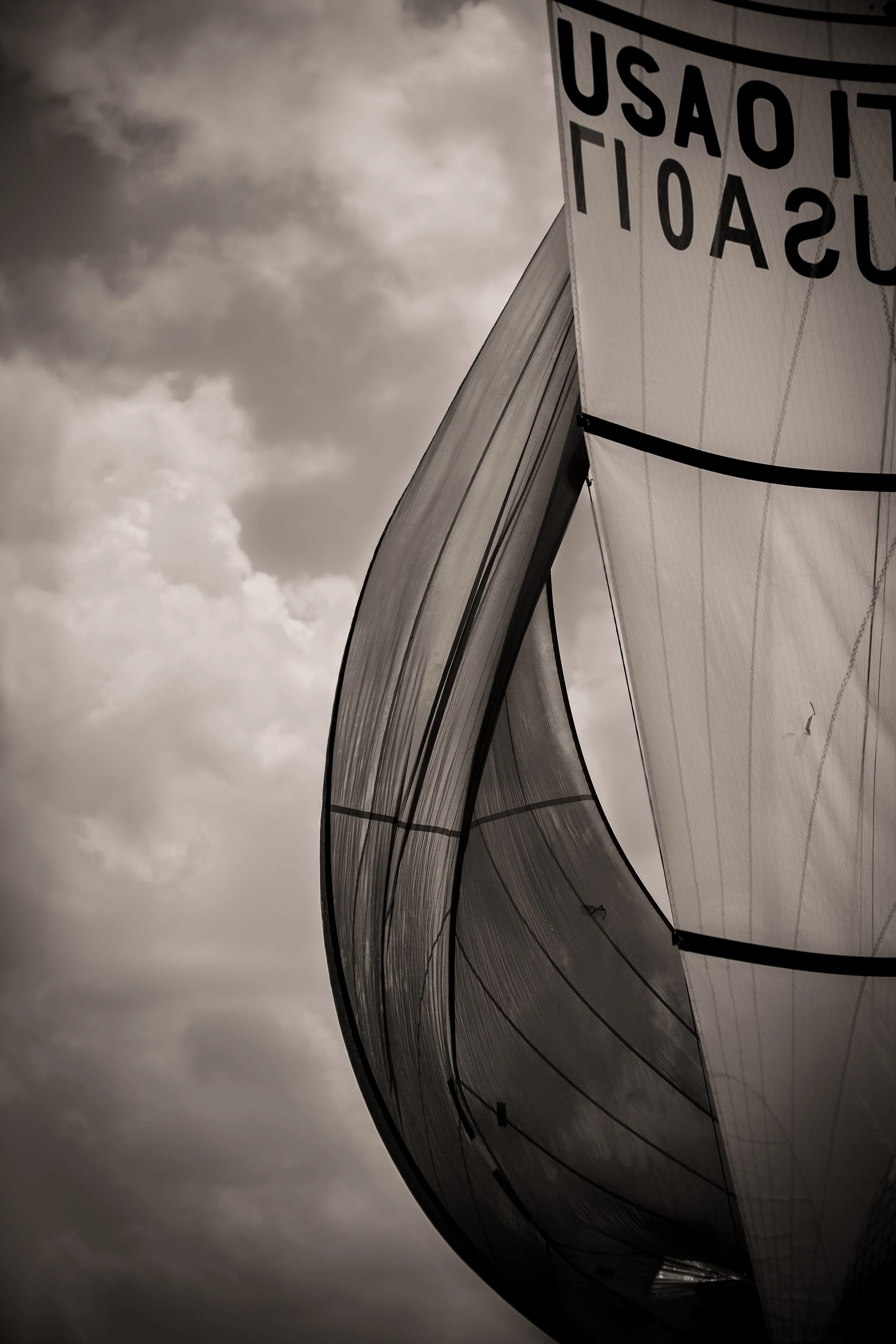 Close-up of a large, modern sailboat or yacht with a curved sail against a cloudy sky.