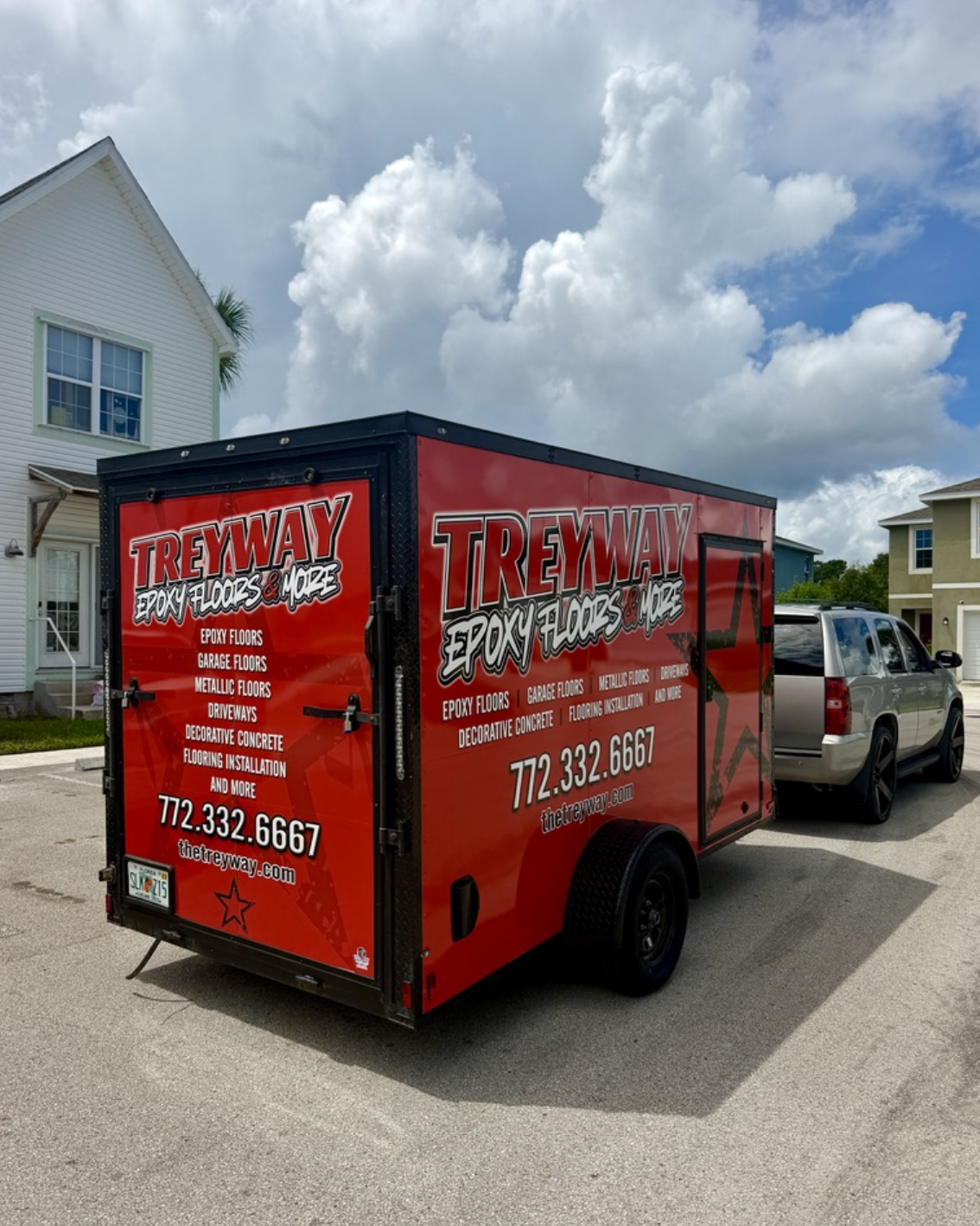 Red trailer advertising Treway epoxy floors and more, parked on a residential street with houses and a partly cloudy sky in the background.