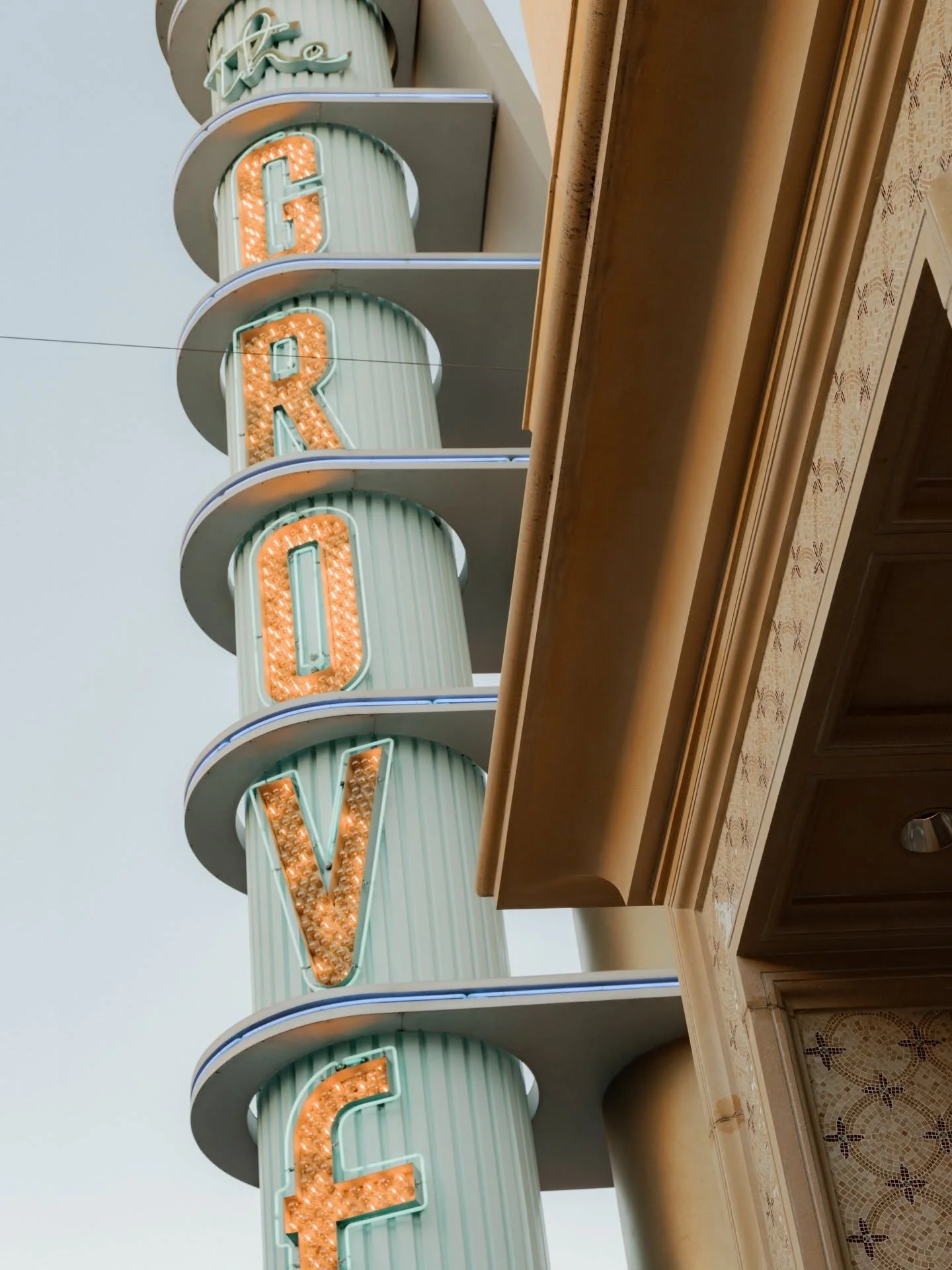 A vintage neon sign spelling out 'HOTEL' with orange bulbs, mounted on a vertical striped light green and white column, with a beige decorative cornice below and a cloudy sky in the background.