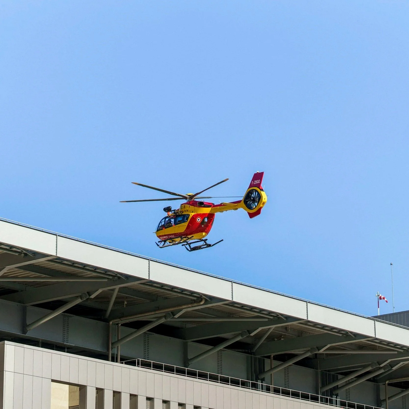 A yellow and red helicopter hovering near a building with a blue sky background, and a Canadian flag flying nearby.