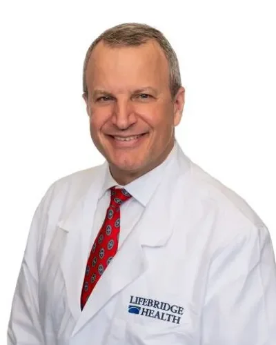 A male doctor wearing a white coat with the Lifebridge Health logo, smiling, with a white background.