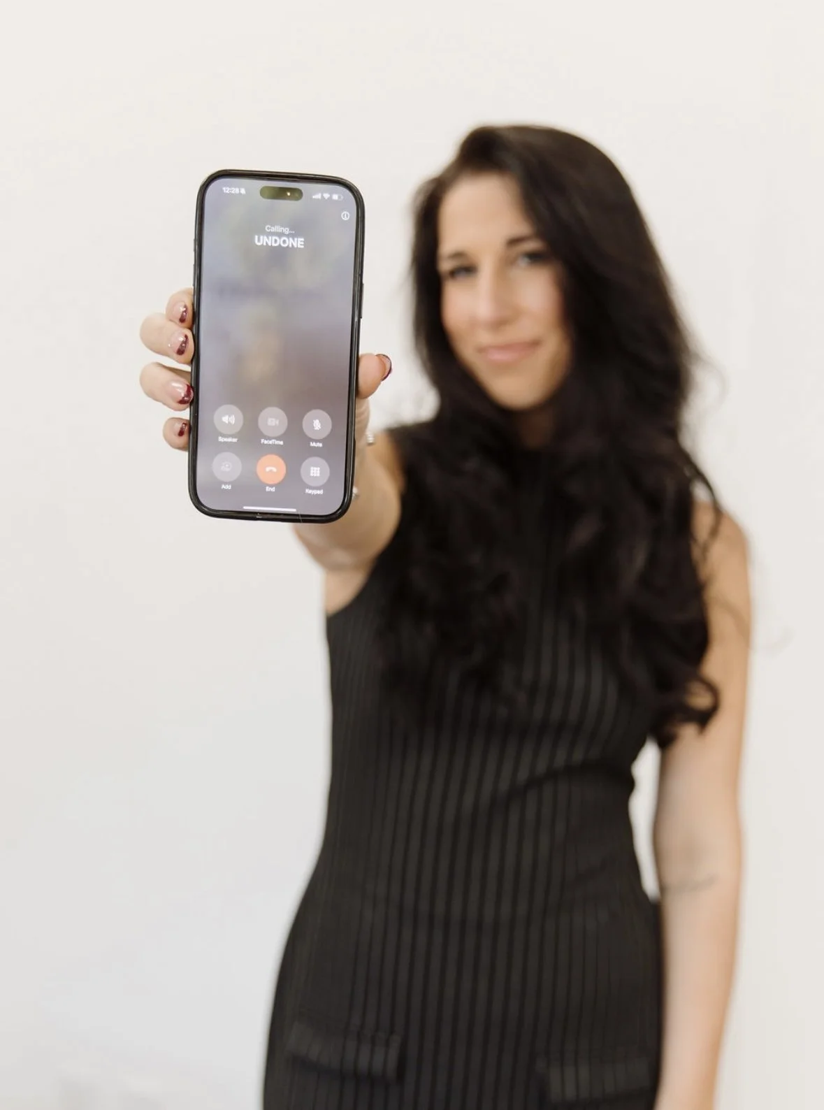 Woman holding a smartphone showing an ongoing call with the contact name 'UNDONE'.