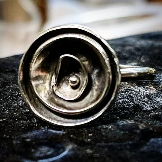 Close-up of a metal bottle opener shaped like a battery opening, placed on a dark surface.