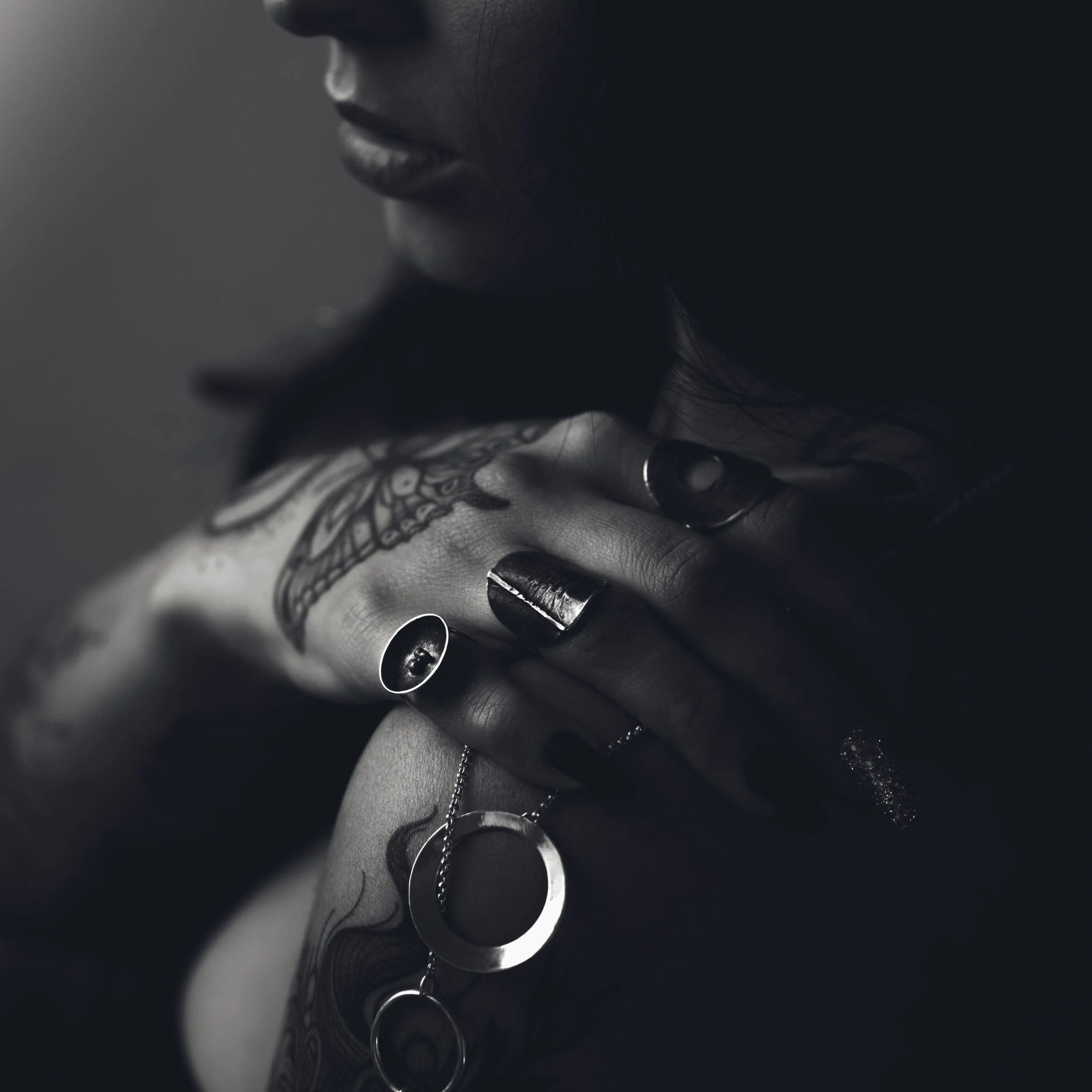 Close-up of a person's lips, tattooed hand, and silver jewelry, with a dark background.
