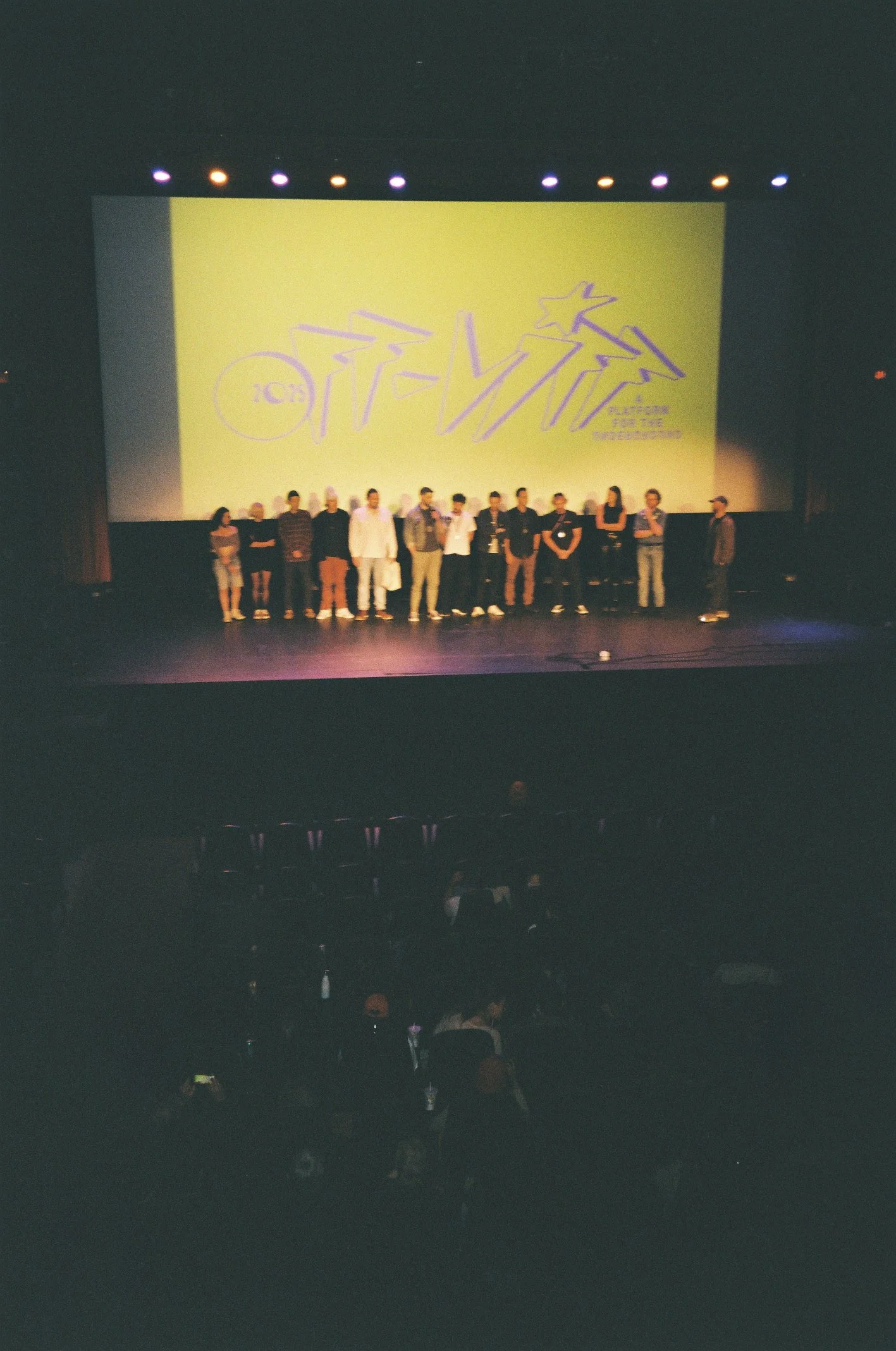 People standing in front of a large screen on stage in a theater.