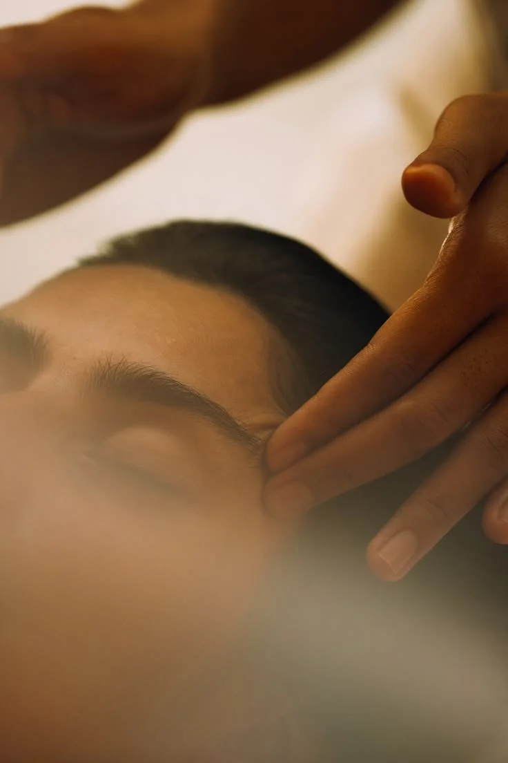 Une personne reçoit un massage du visage, allongée avec un massage de la main sur le front.