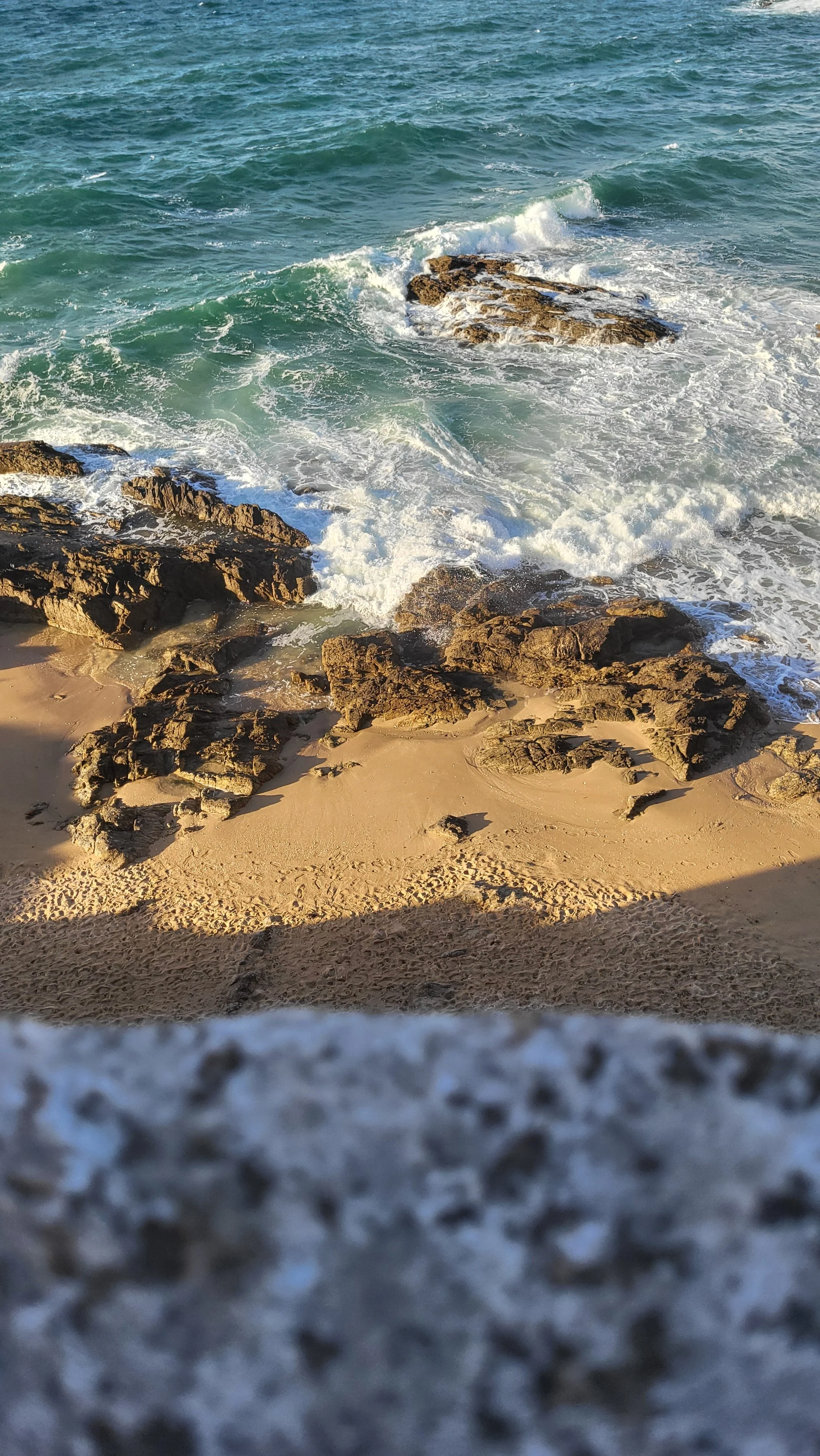 Vague de mer frappant des rochers sur une plage ensoleillée.