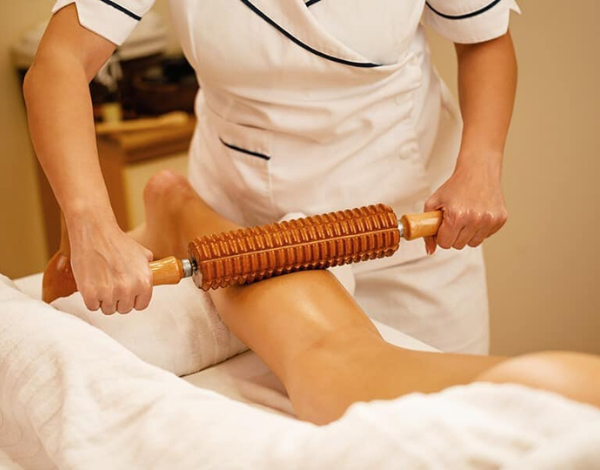 Une personne reçoit un massage avec un rouleau en bois sur la cuisse.