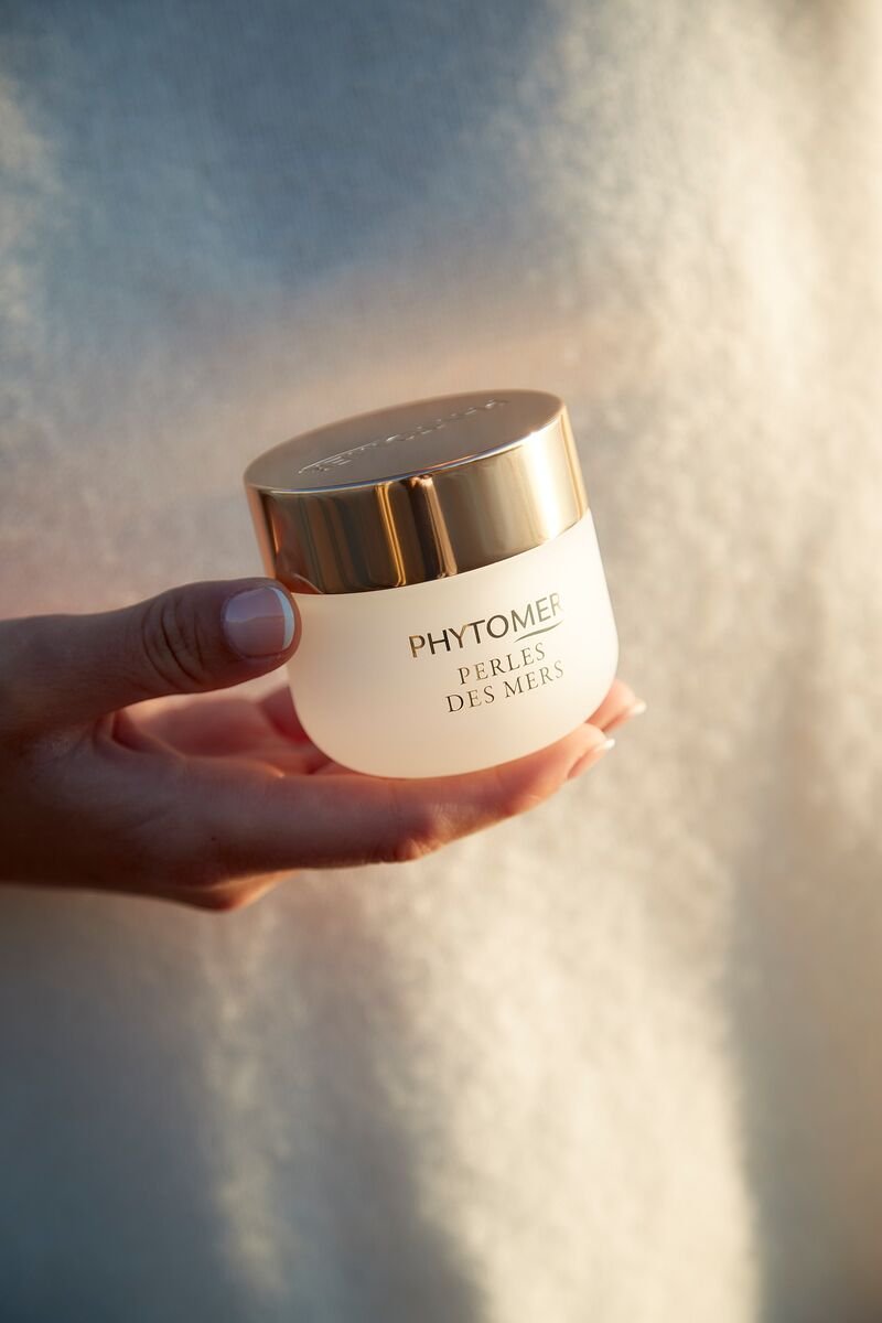 Une main tient un pot de crème de la marque Phytomer, nommé Perles des Mers, avec un fond neutre.