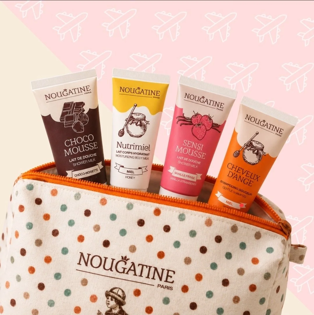 Différentes bouteilles de produits pour la douche et le corps de la marque Nougatine, dans une trousse à rayures avec pois, fond rose avec dessins d'avions.